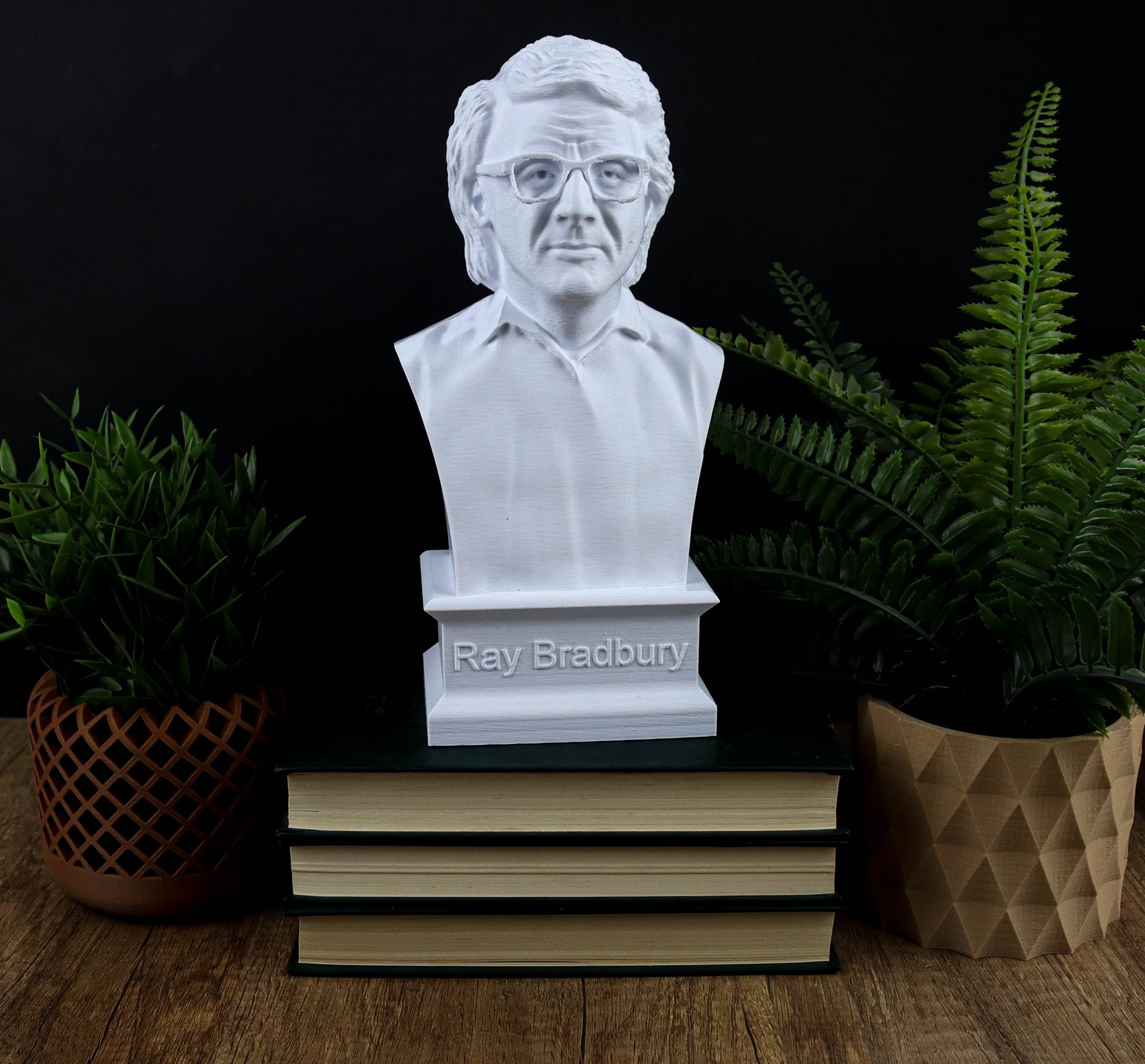 A bust of Ray Bradbury, a renowned American author and inventor, is displayed on a stack of books, surrounded by potted plants and a brown paper bag.