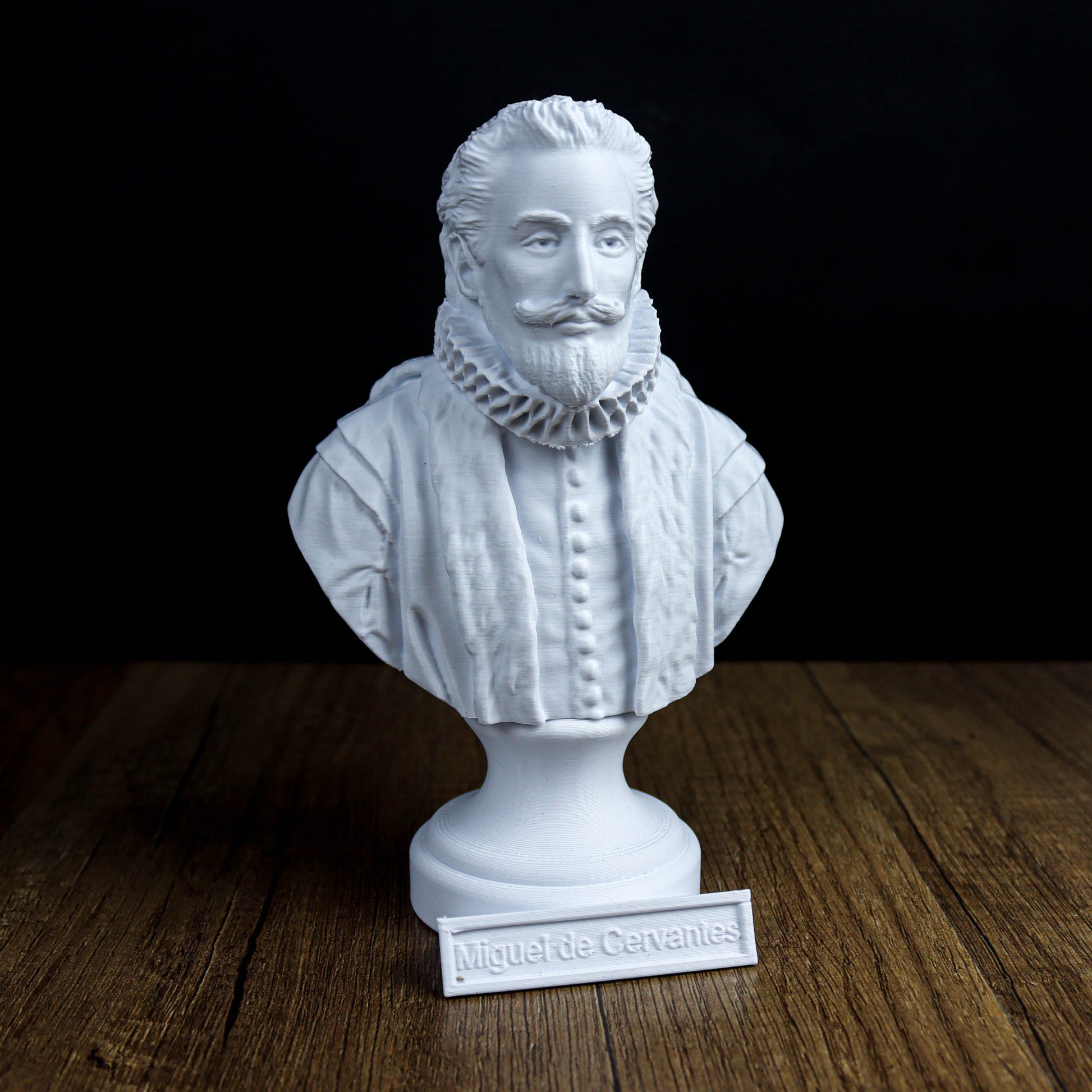 A white bust of a man with a beard and mustache, wearing a ruffled collar, is displayed on a wooden surface.