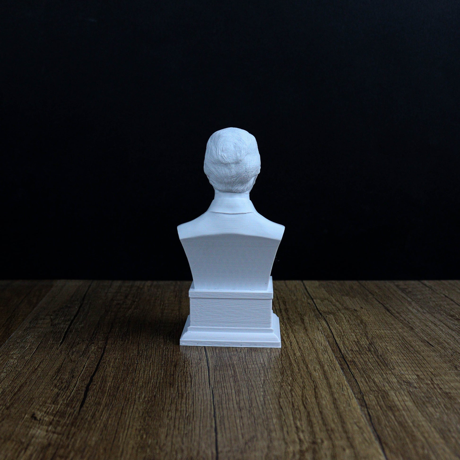 A white bust sculpture is displayed on a wooden surface against a dark background.