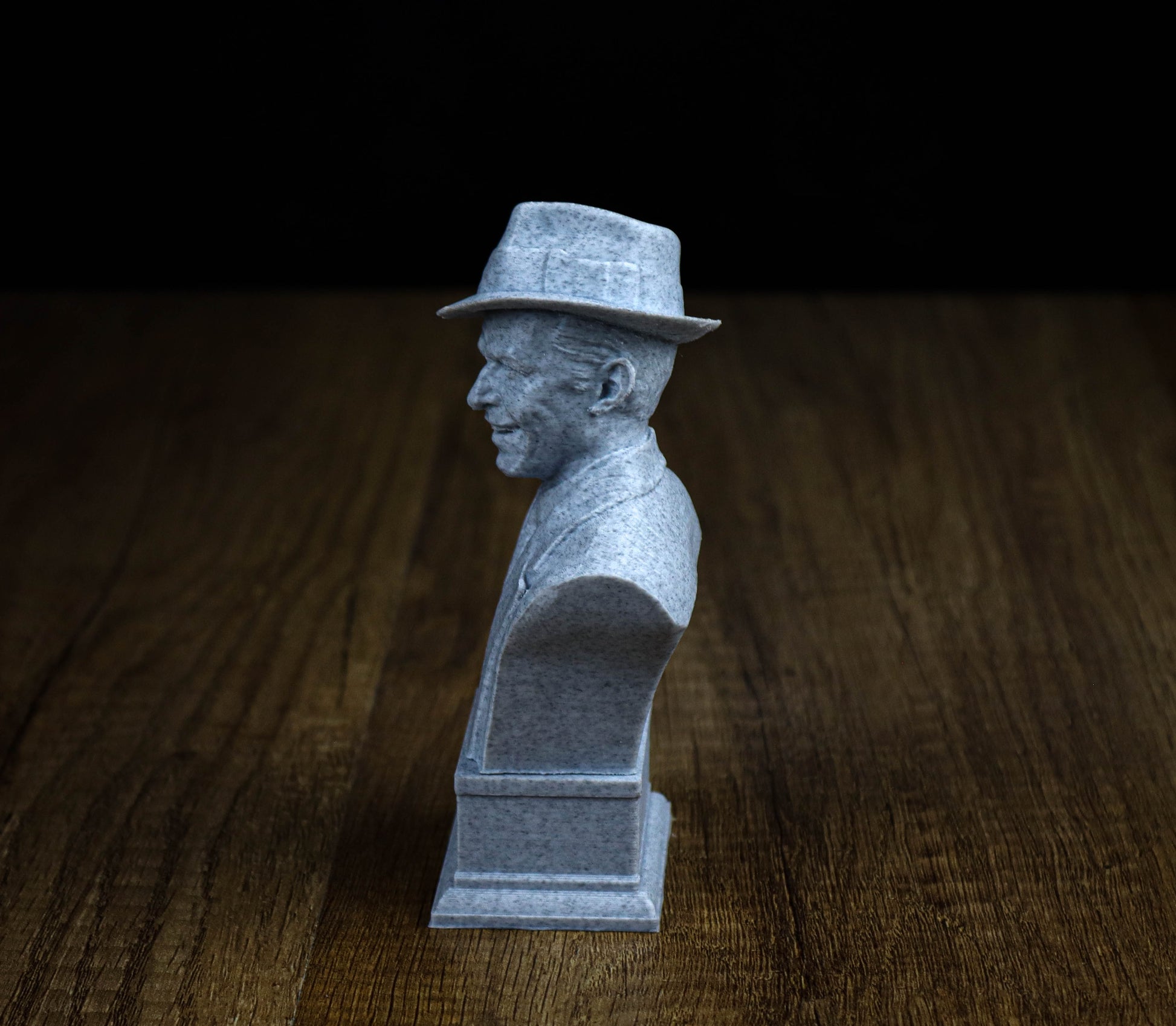 A small gray bust of a man wearing a hat, sitting on a wooden surface.