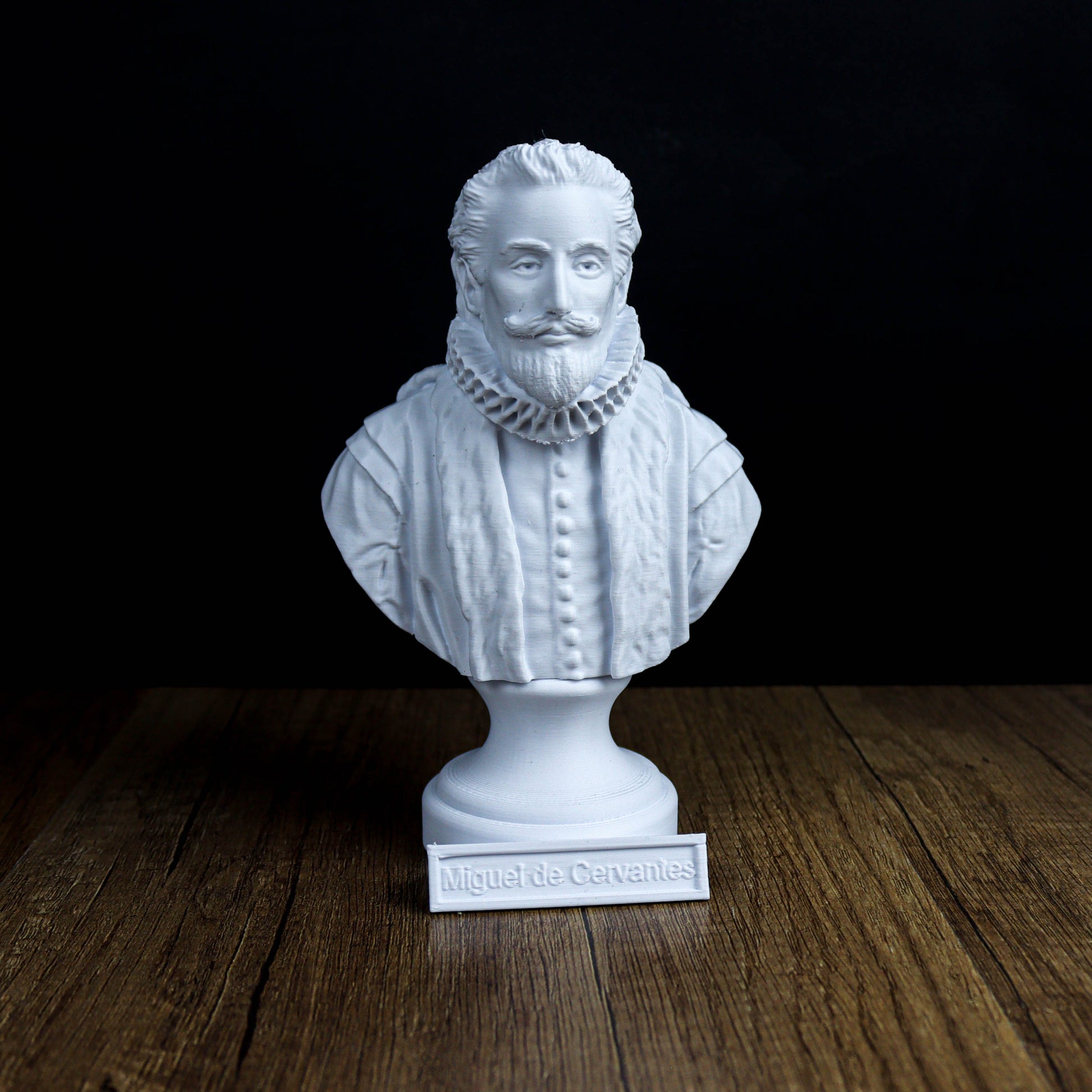 A white bust of a bearded man wearing a ruffled collar, standing on a wooden surface with a plaque that reads "Miguel de Cervantes".