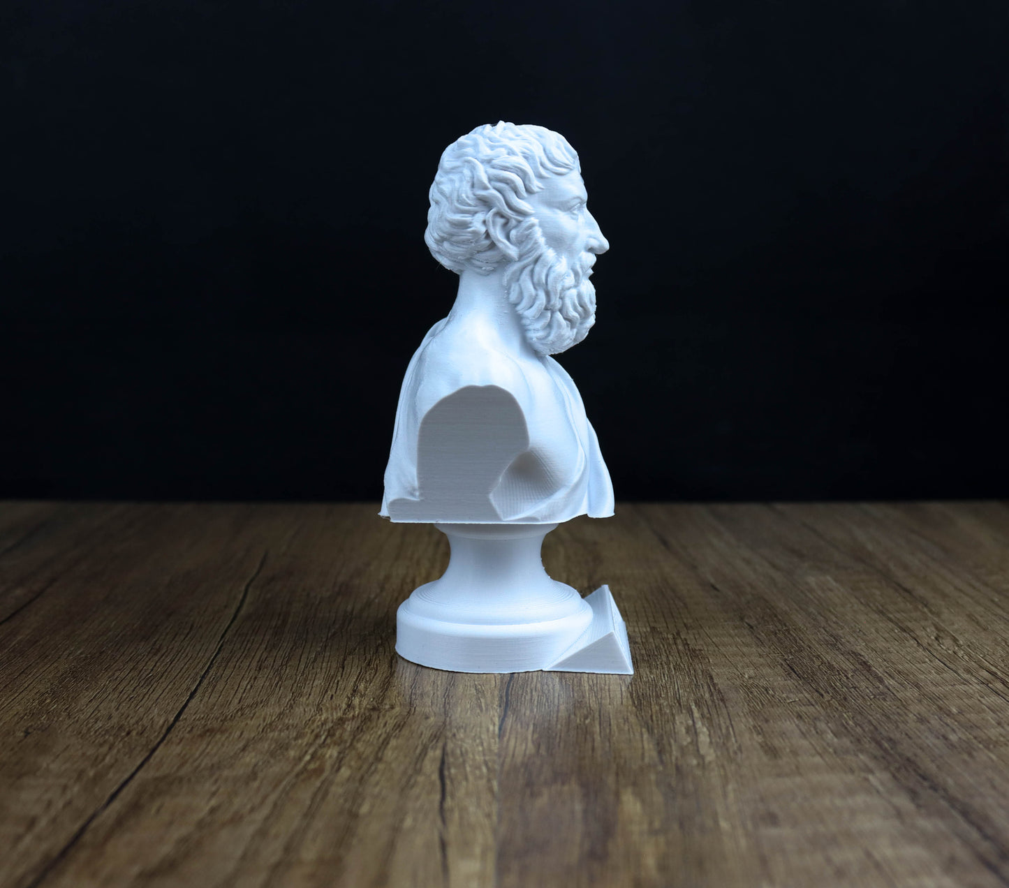A white bust of a bearded man is displayed on a wooden surface against a dark background.
