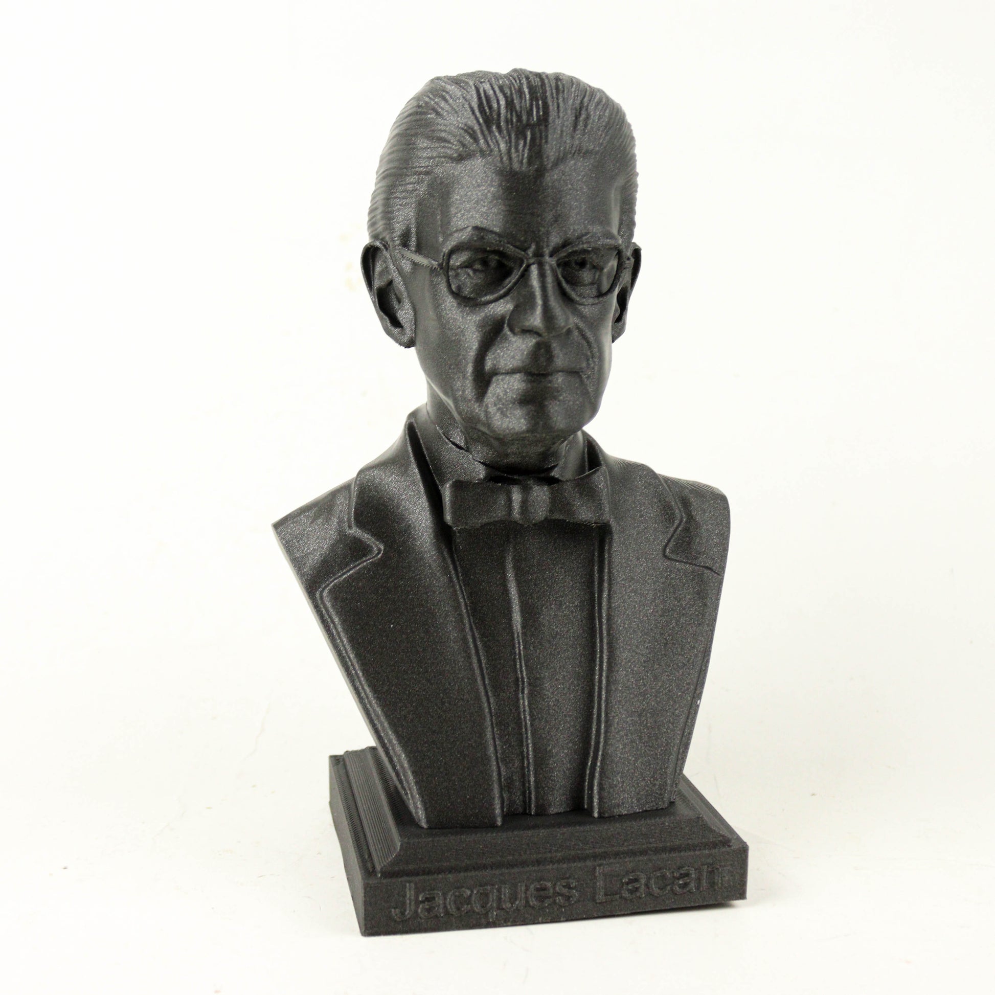 A black bust sculpture of a man wearing a suit and bow tie, with the name "Jacques Lacan" engraved on the base.