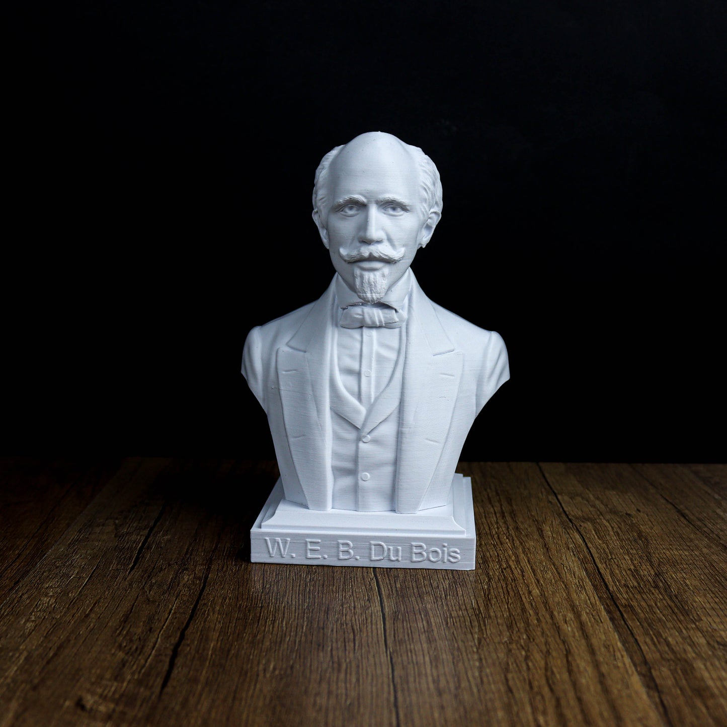 A white bust of a man with a mustache and a formal suit, standing on a wooden surface.