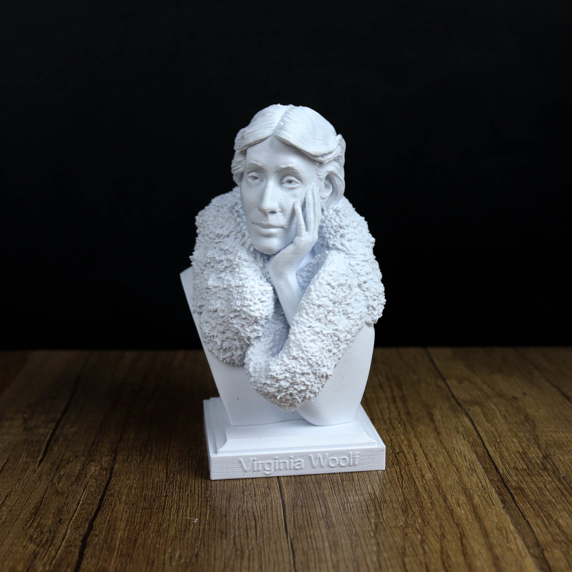 A white bust of a woman with a pensive expression, wearing a fur coat, is displayed on a wooden surface against a black background.