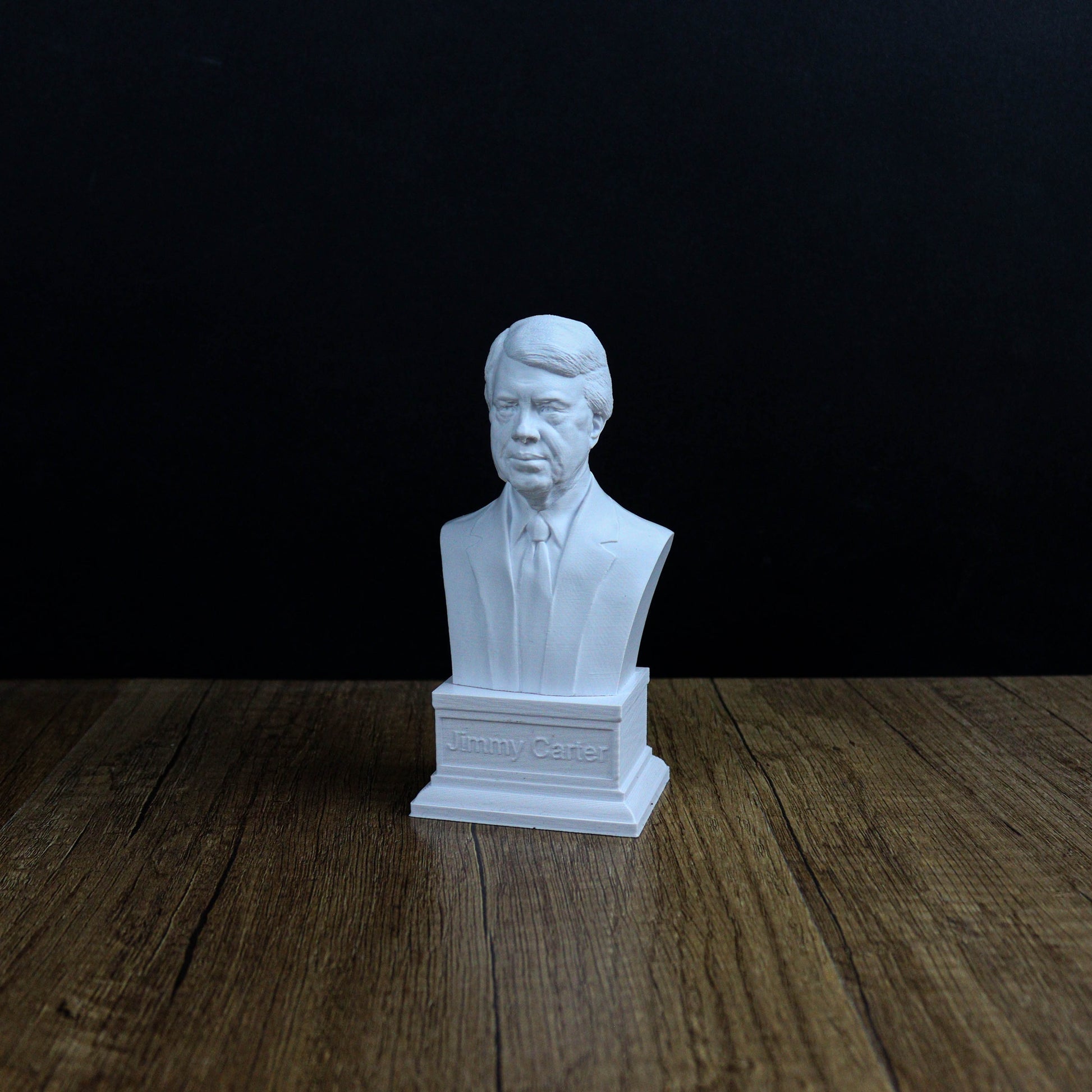 A white bust of a man is displayed on a wooden surface against a black background.