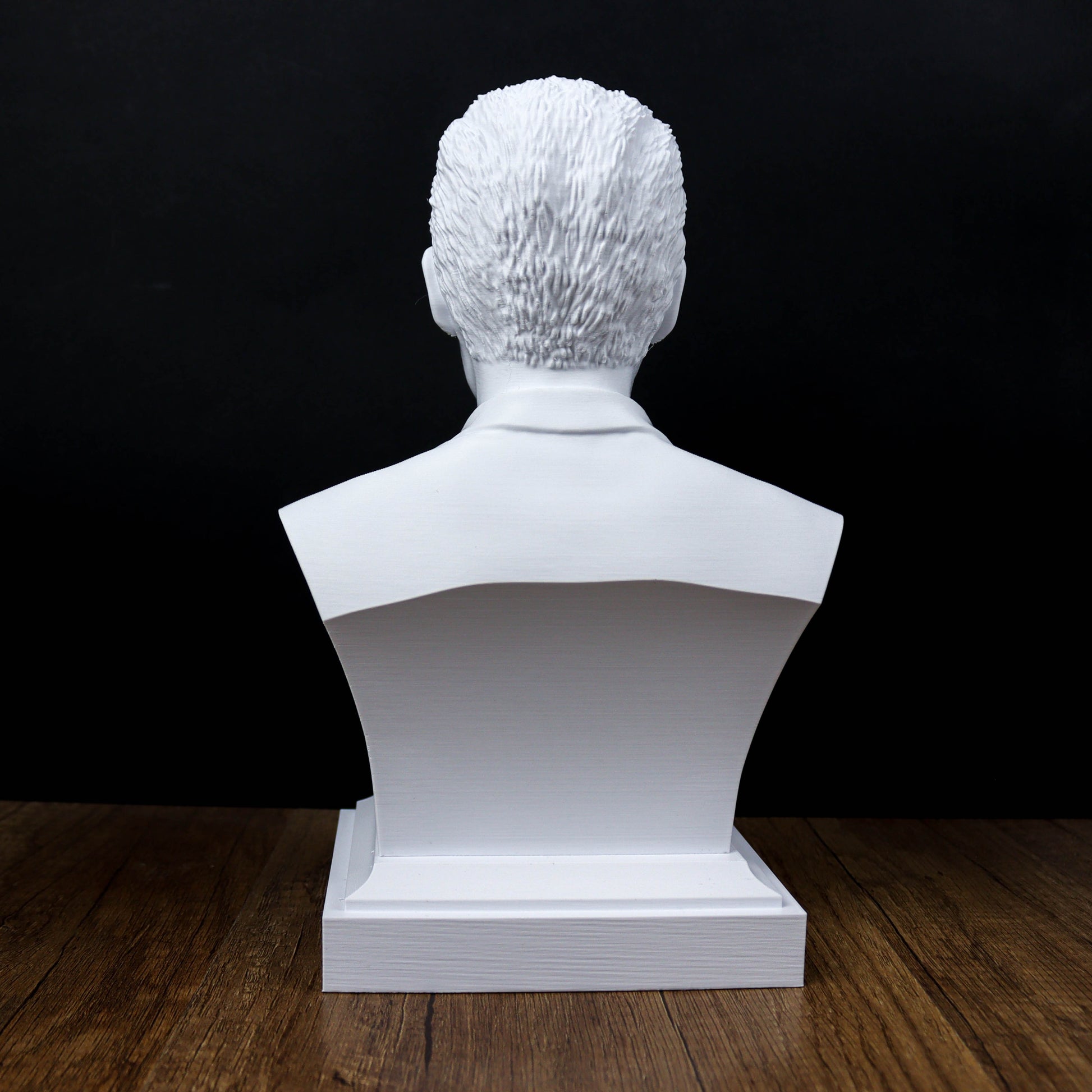 A white bust sculpture of a person's head is displayed on a wooden surface against a black background.