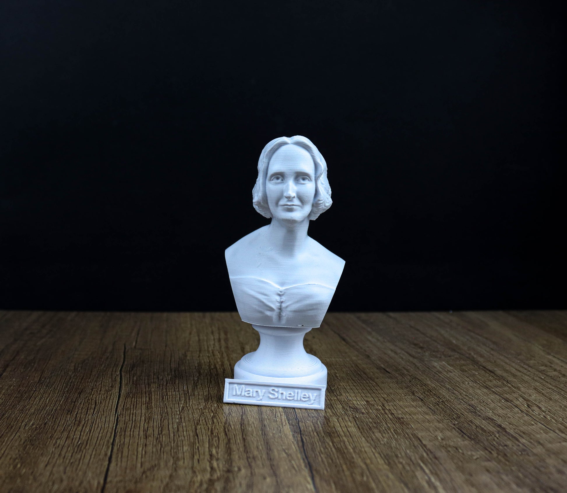 A white bust of a woman is displayed on a wooden surface against a black background.