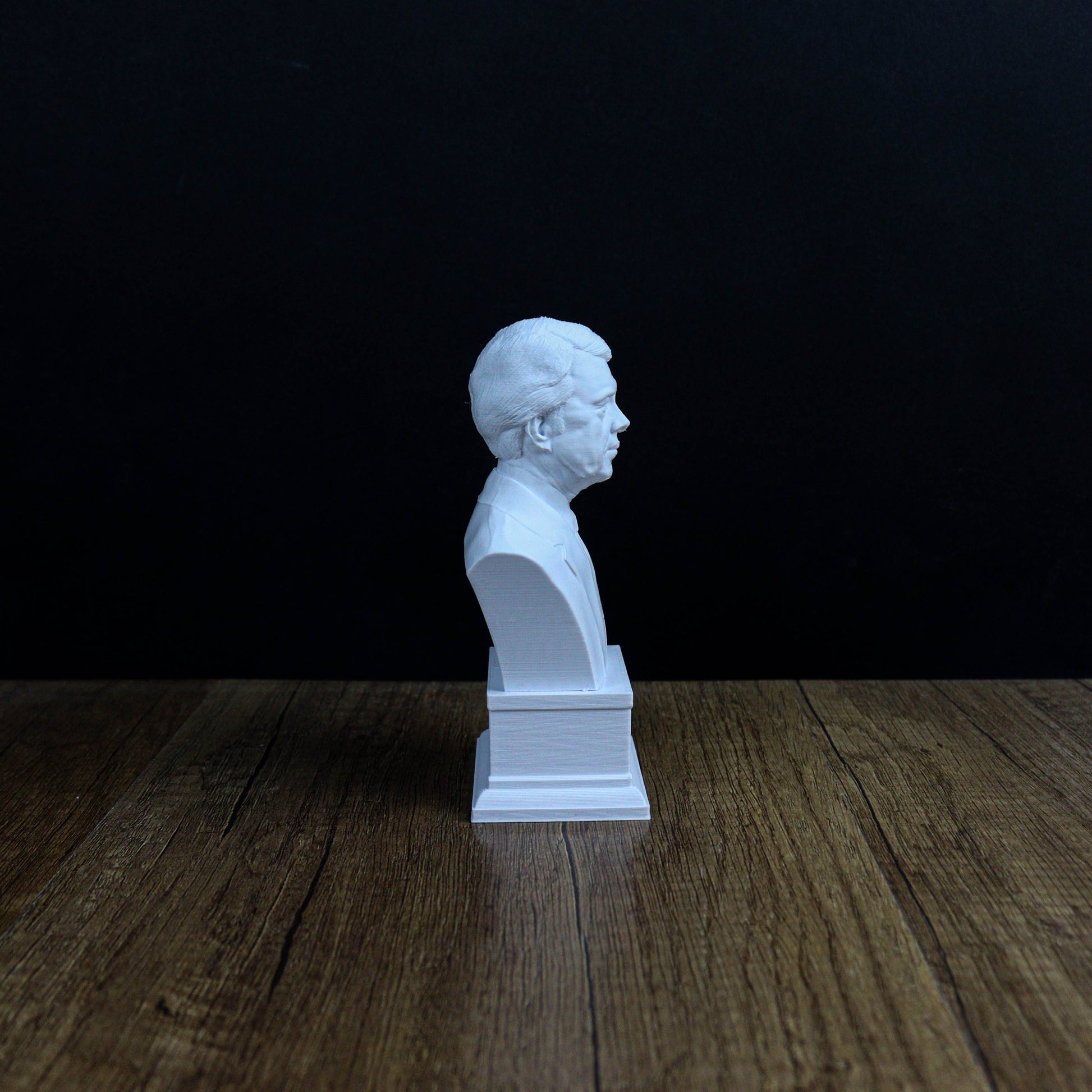 A white bust of a person is sitting on a wooden surface against a dark background.