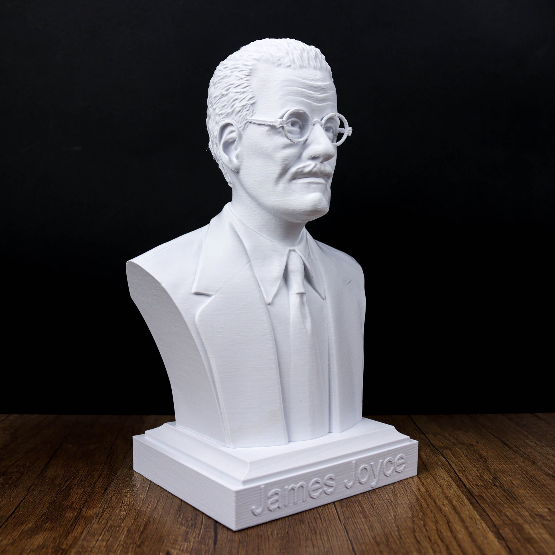 A white bust of a man wearing glasses and a suit, sitting on a wooden surface.