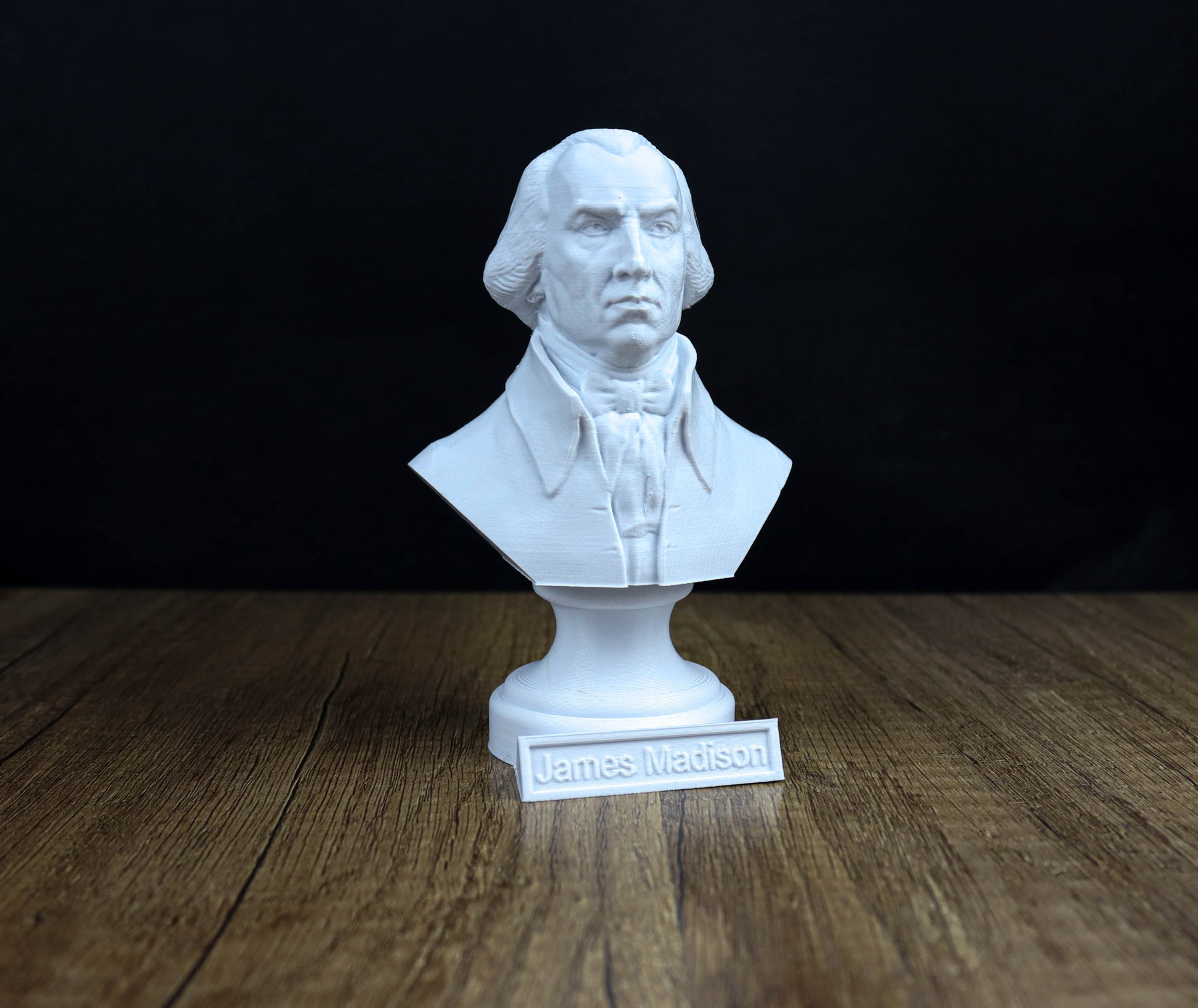 A white bust of a man, likely James Madison, is displayed on a wooden surface with a nameplate below it.