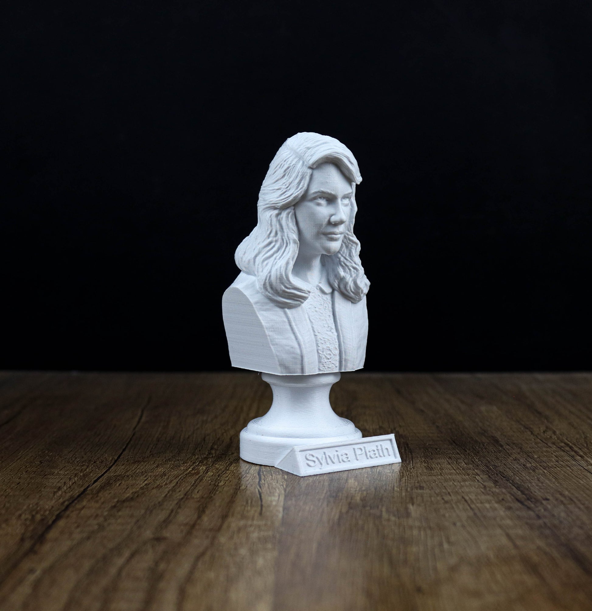 A white bust of a woman with long hair is displayed on a wooden surface against a black background.