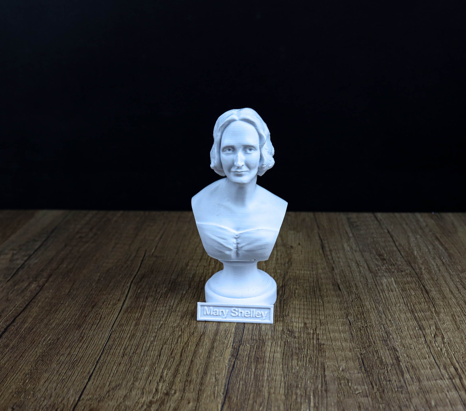 A white bust of a woman is displayed on a wooden surface, with the name "Mary Shelley" written below it.