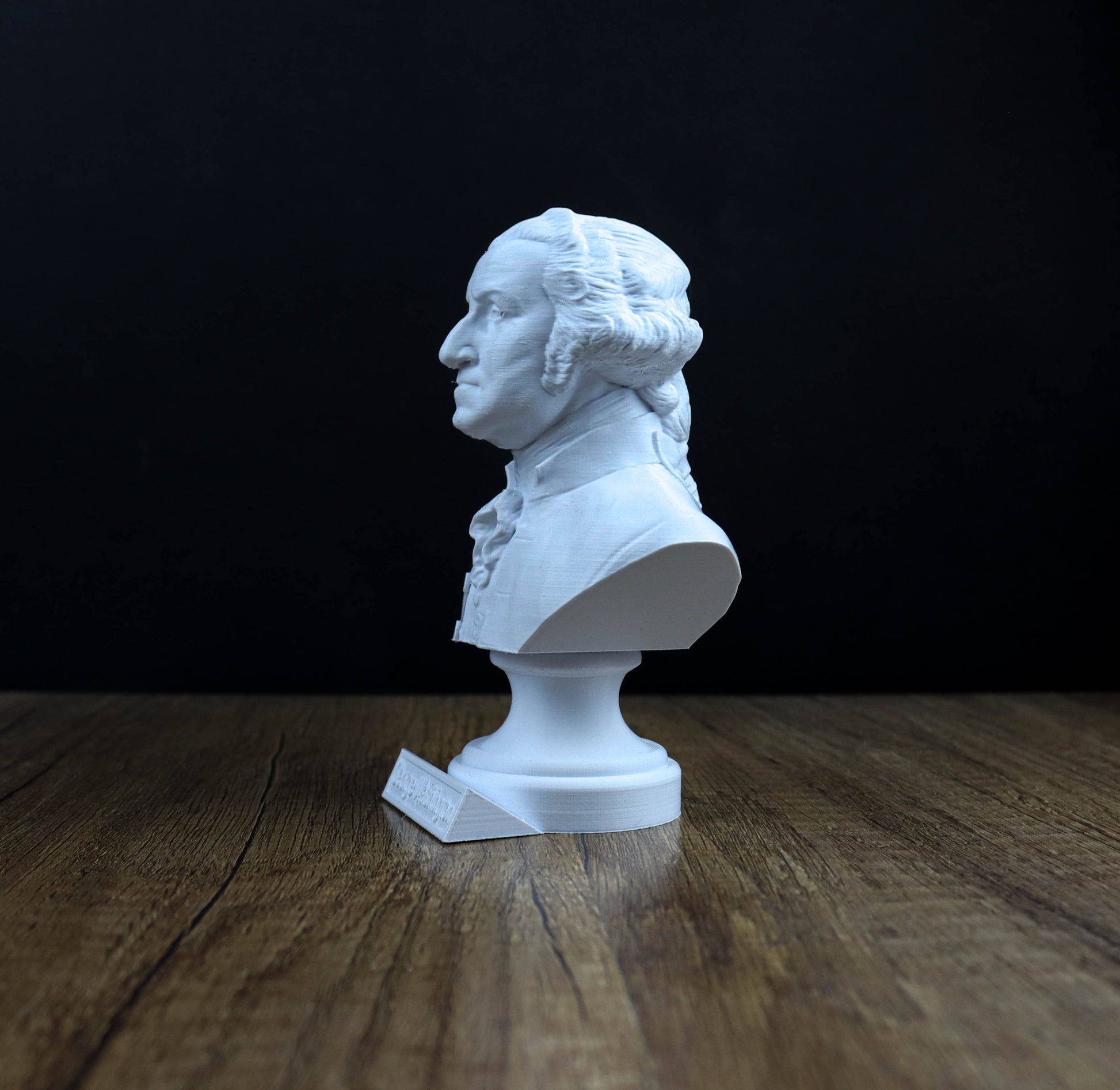 A white bust of George Washington, the first President of the United States, is displayed on a wooden surface against a dark background.