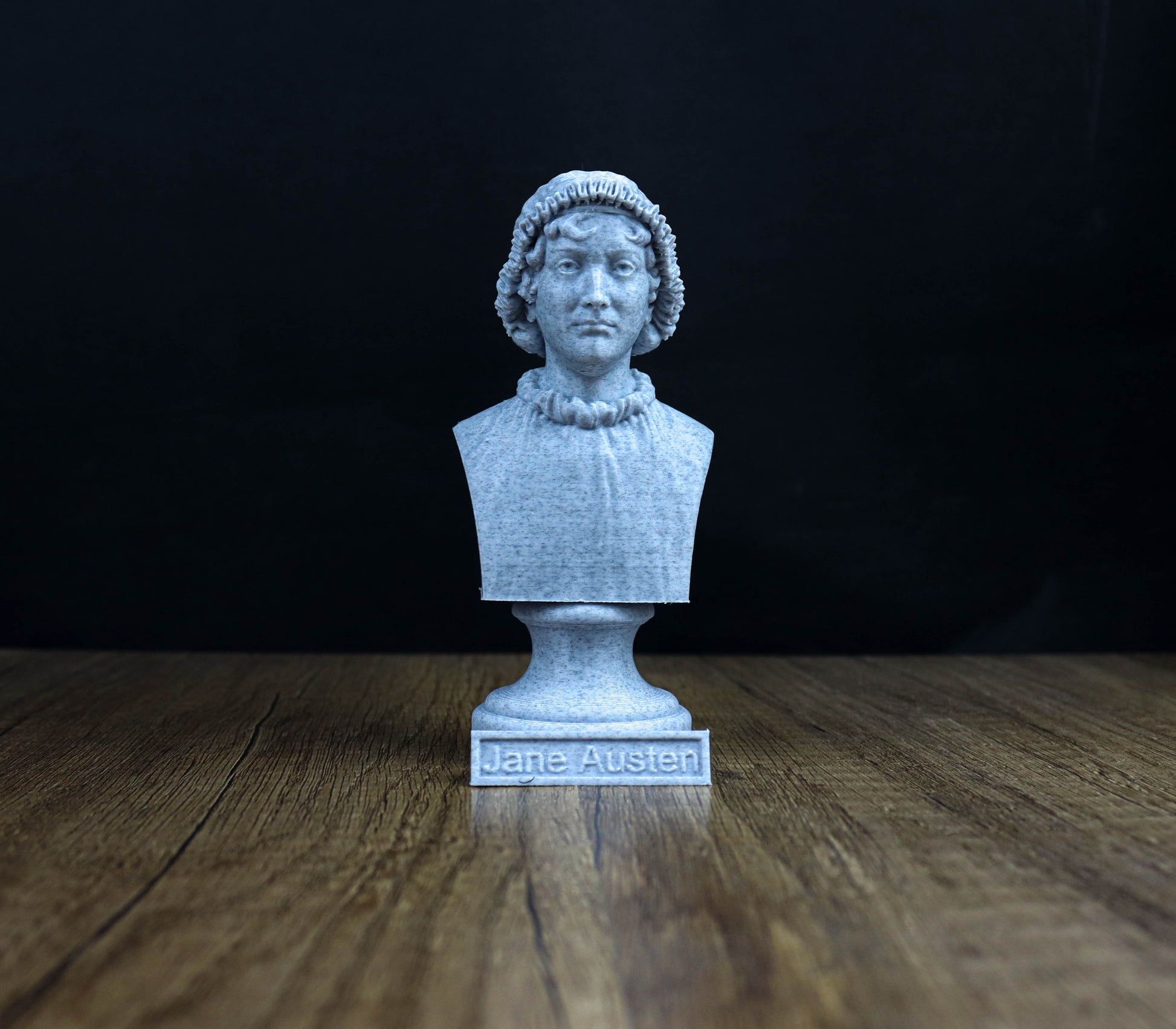 A small bust of a person, likely a historical figure, is displayed on a wooden surface against a dark background.