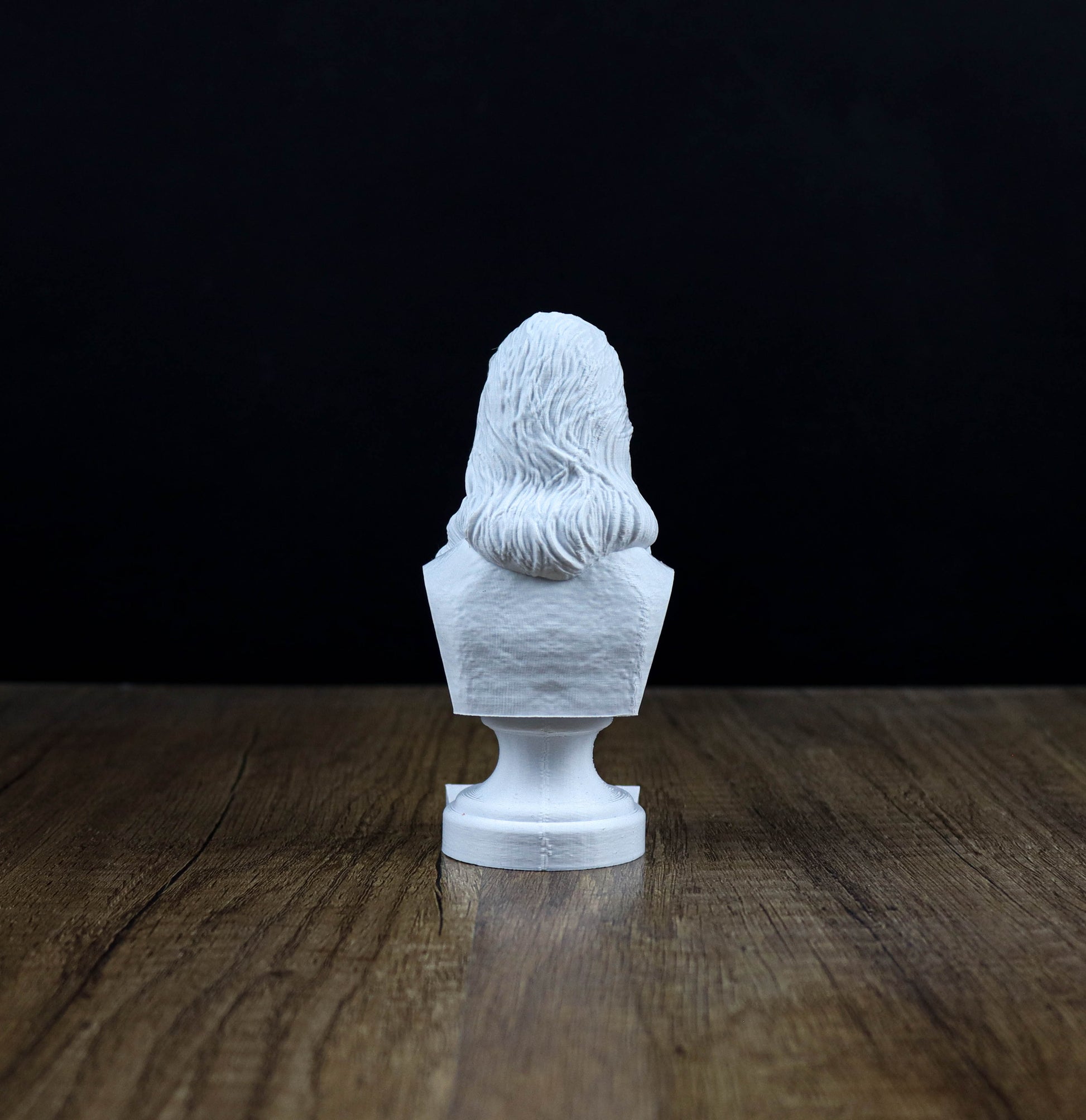 A white bust of a person is sitting on a wooden surface against a dark background.