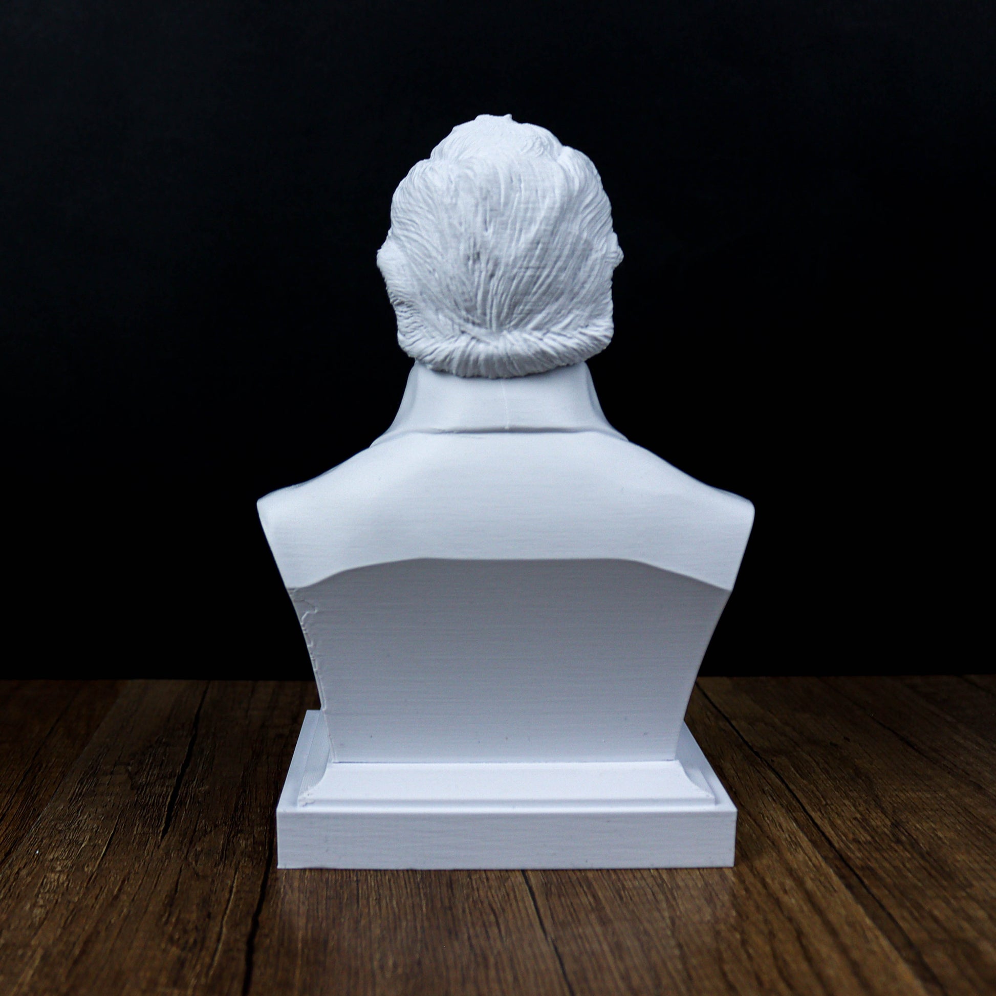 A white bust sculpture of a person's head is displayed on a wooden surface against a dark background.