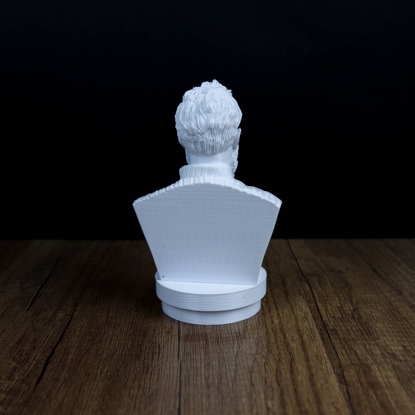 A white bust sculpture is displayed on a wooden surface against a dark background.
