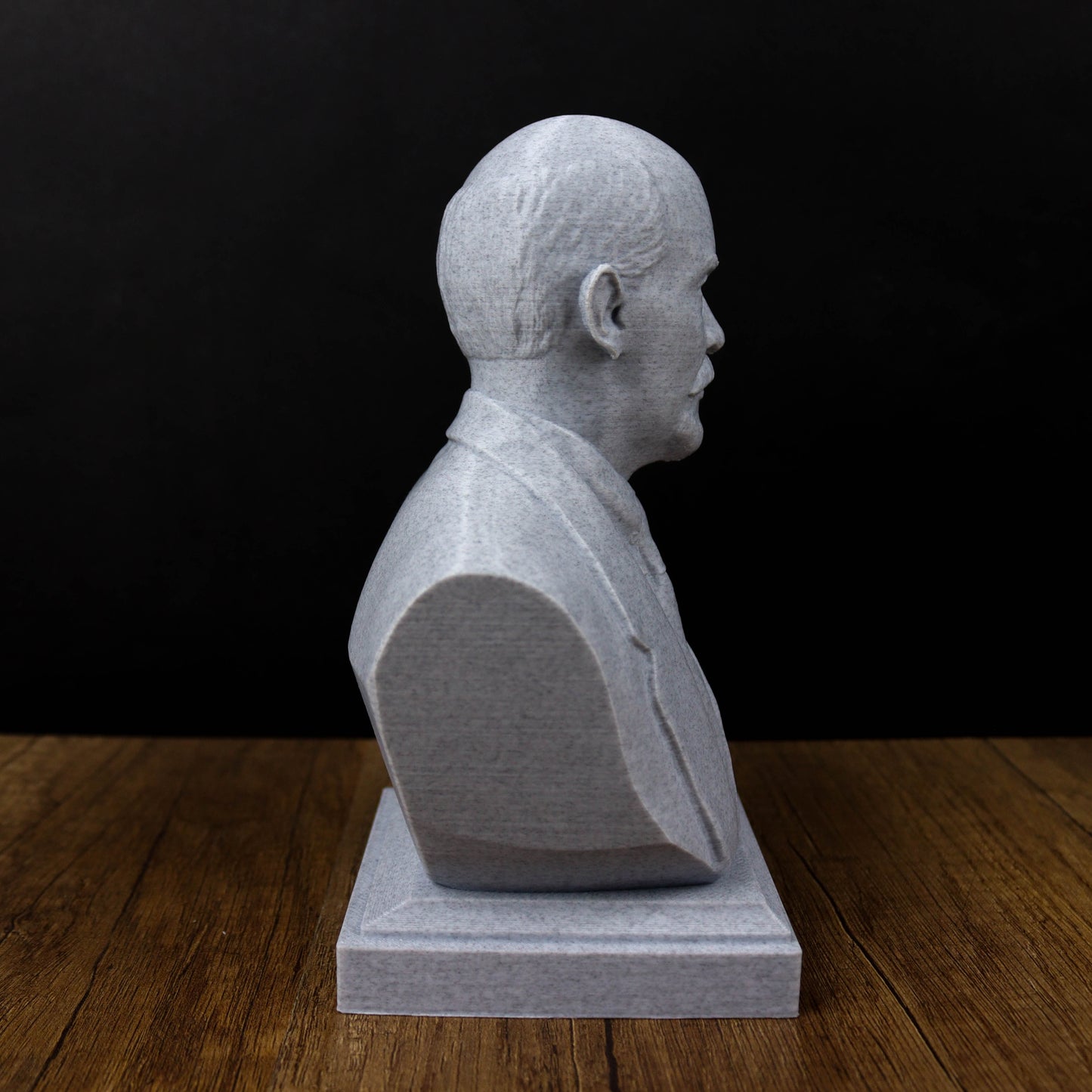 A white bust of a man is displayed on a wooden surface against a black background.