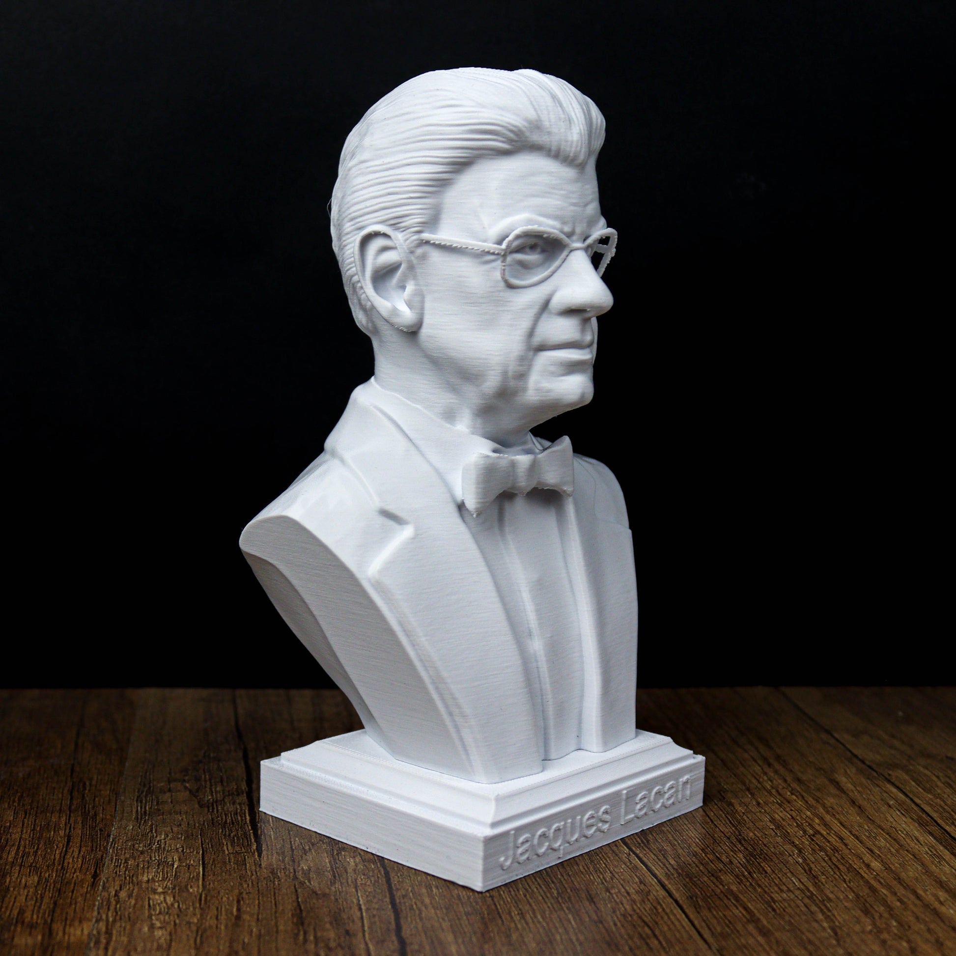 A white bust of a man wearing a suit and bow tie, sitting on a wooden surface.