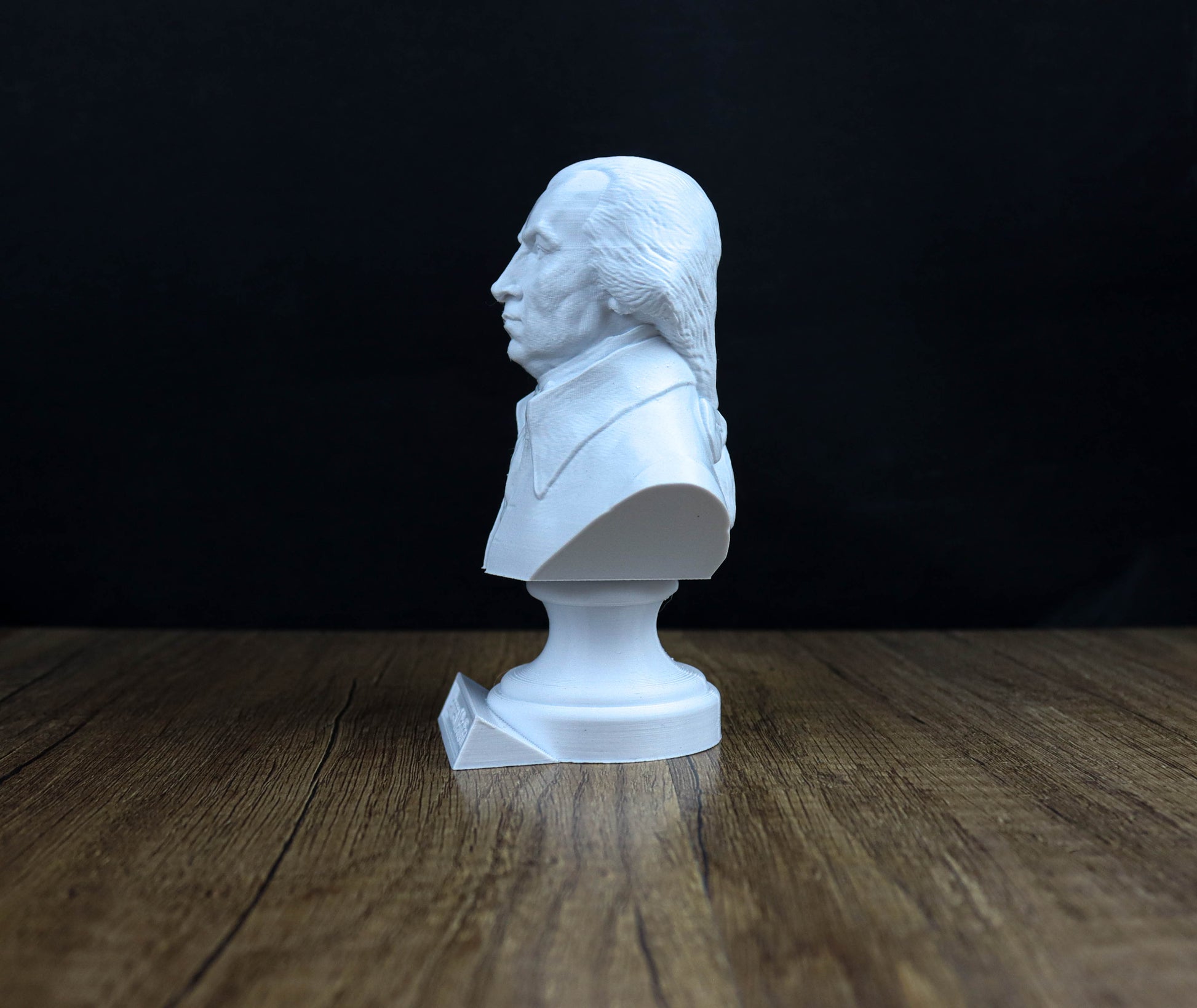 A white bust of a man is sitting on a wooden surface against a dark background.