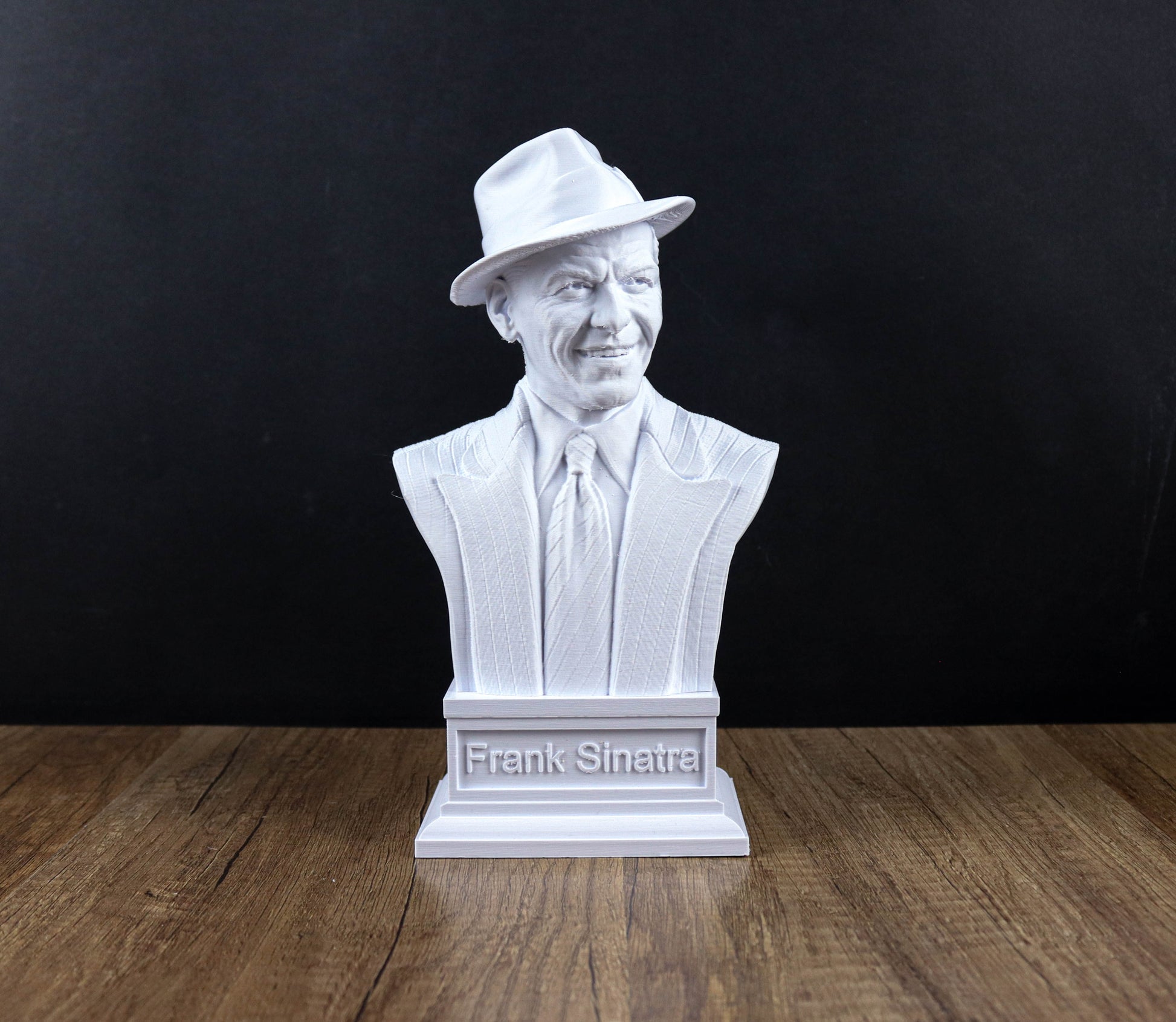 A white bust of Frank Sinatra, a famous American singer, is displayed on a wooden surface against a black background.