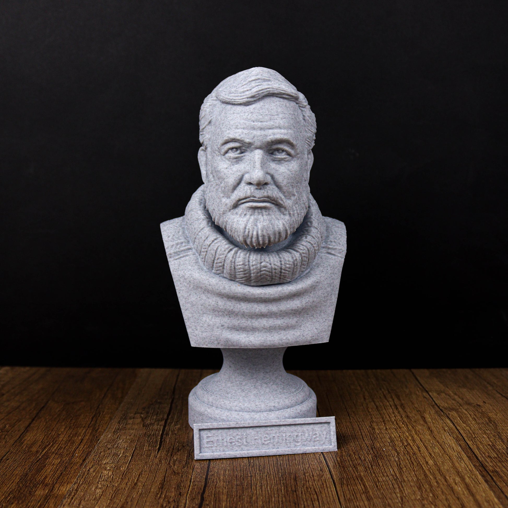 A gray stone bust of a bearded man with a serious expression, placed on a wooden surface against a black background.
