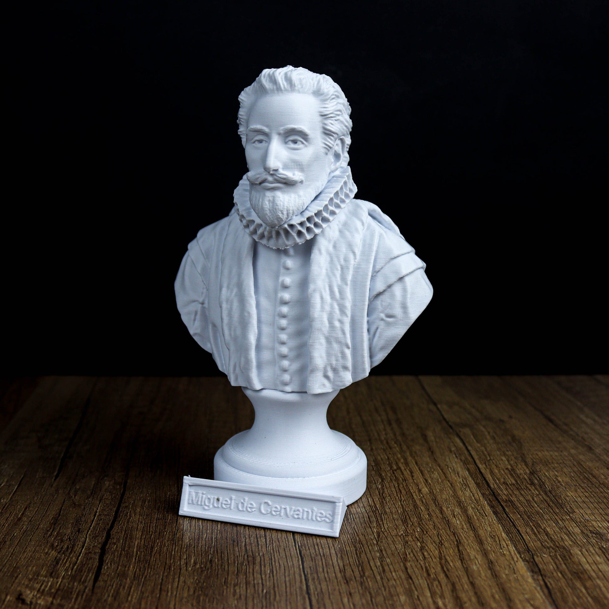 A white bust of a bearded man wearing a ruffled collar, sitting on a wooden surface with a plaque below it that reads "Miguel de Cervantes".