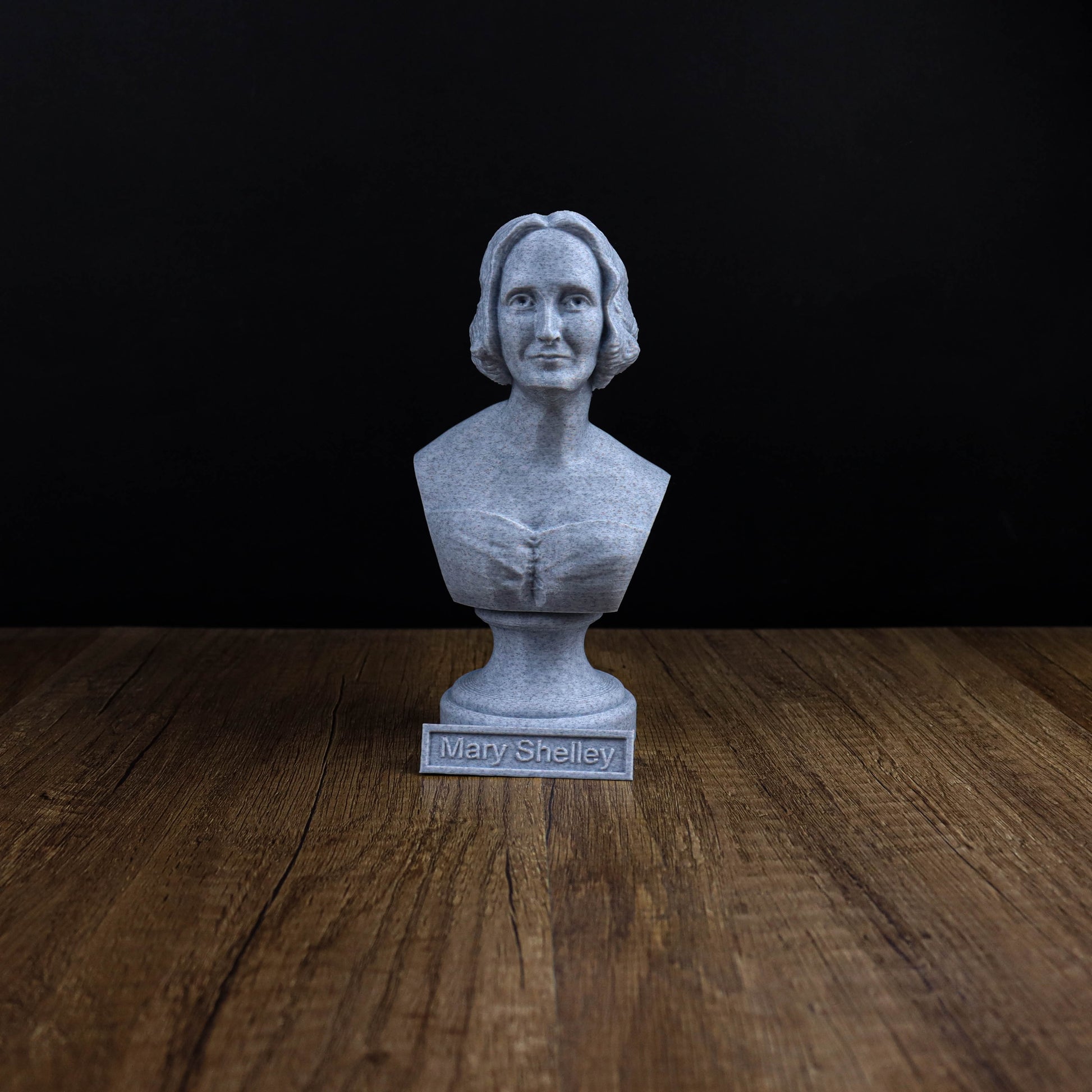 A bust of a person, likely Mary Shelley, is displayed on a wooden surface against a black background.
