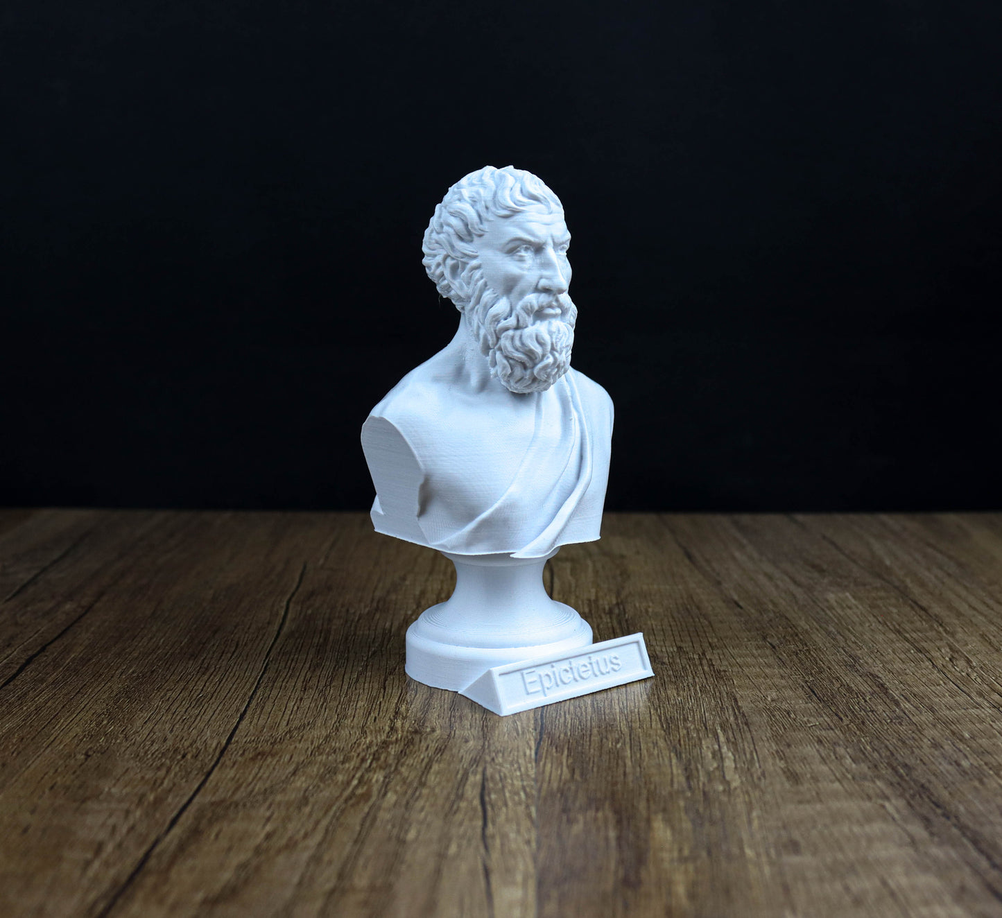 A white bust of a bearded man, likely depicting the Greek poet Epidaurus, is displayed on a wooden surface against a black background.