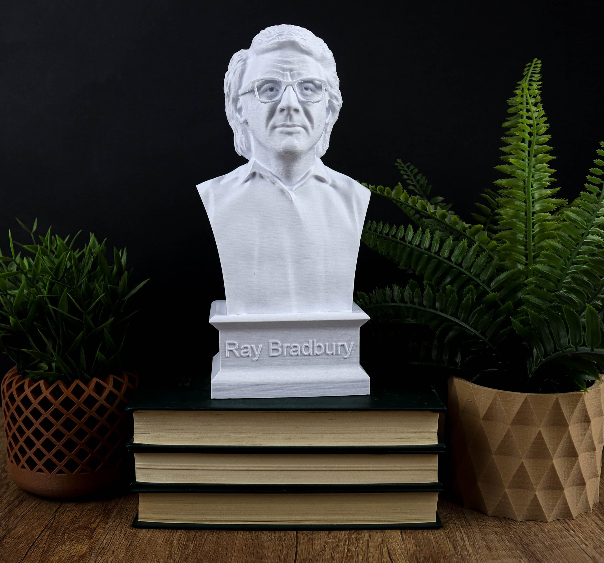 A bust of Ray Bradbury, a famous American author and inventor, is displayed on a stack of books, surrounded by potted plants.
