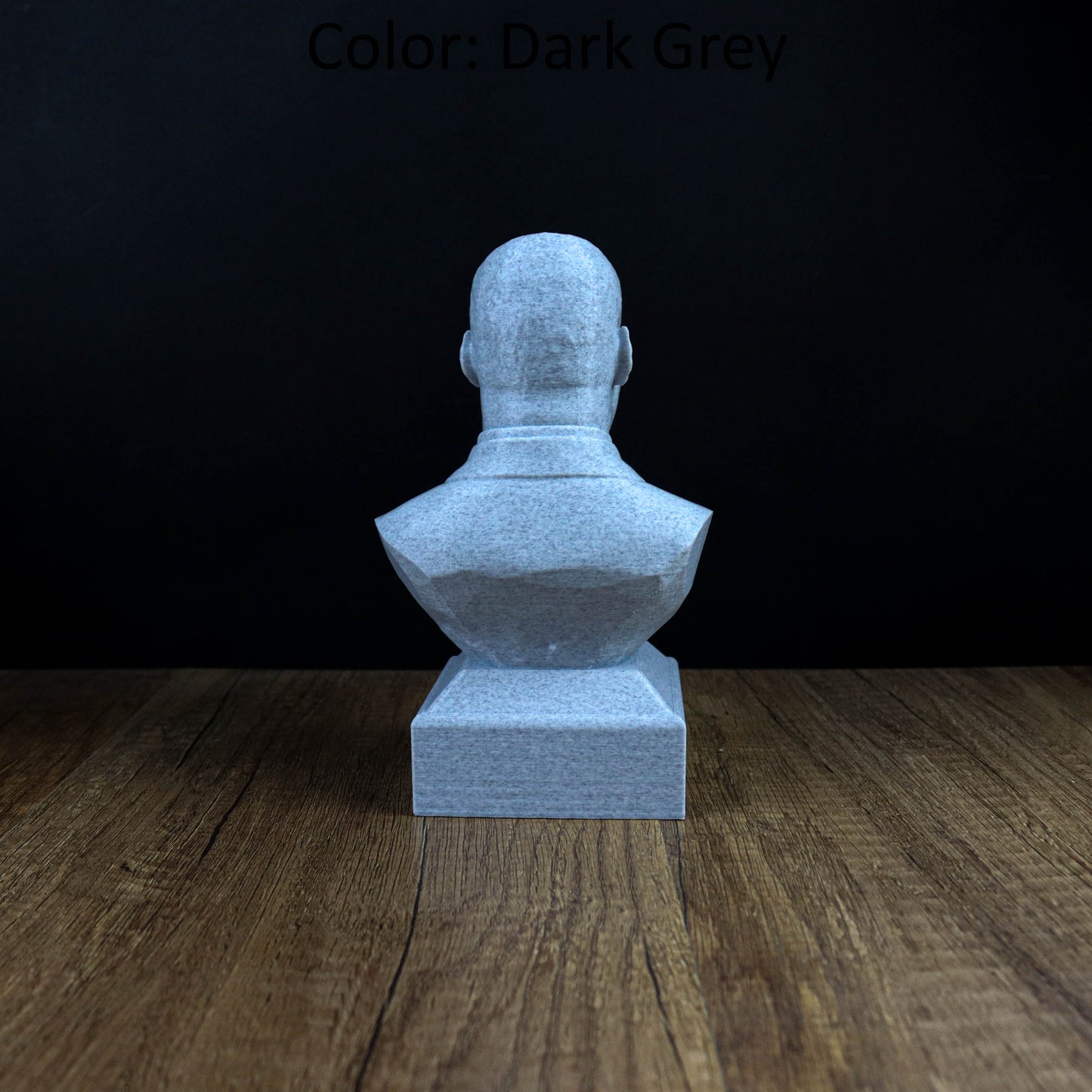 A gray stone bust sculpture is displayed on a wooden surface against a dark background.