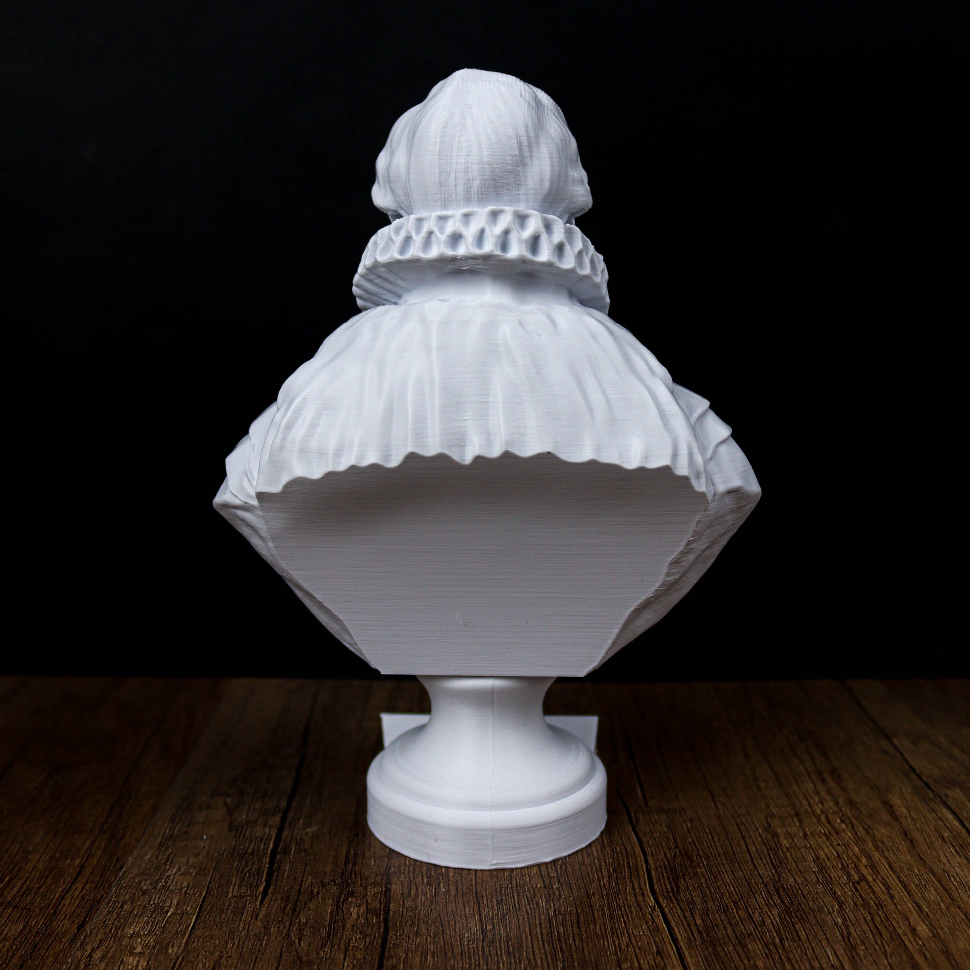 A white bust sculpture is displayed on a wooden surface against a dark background.