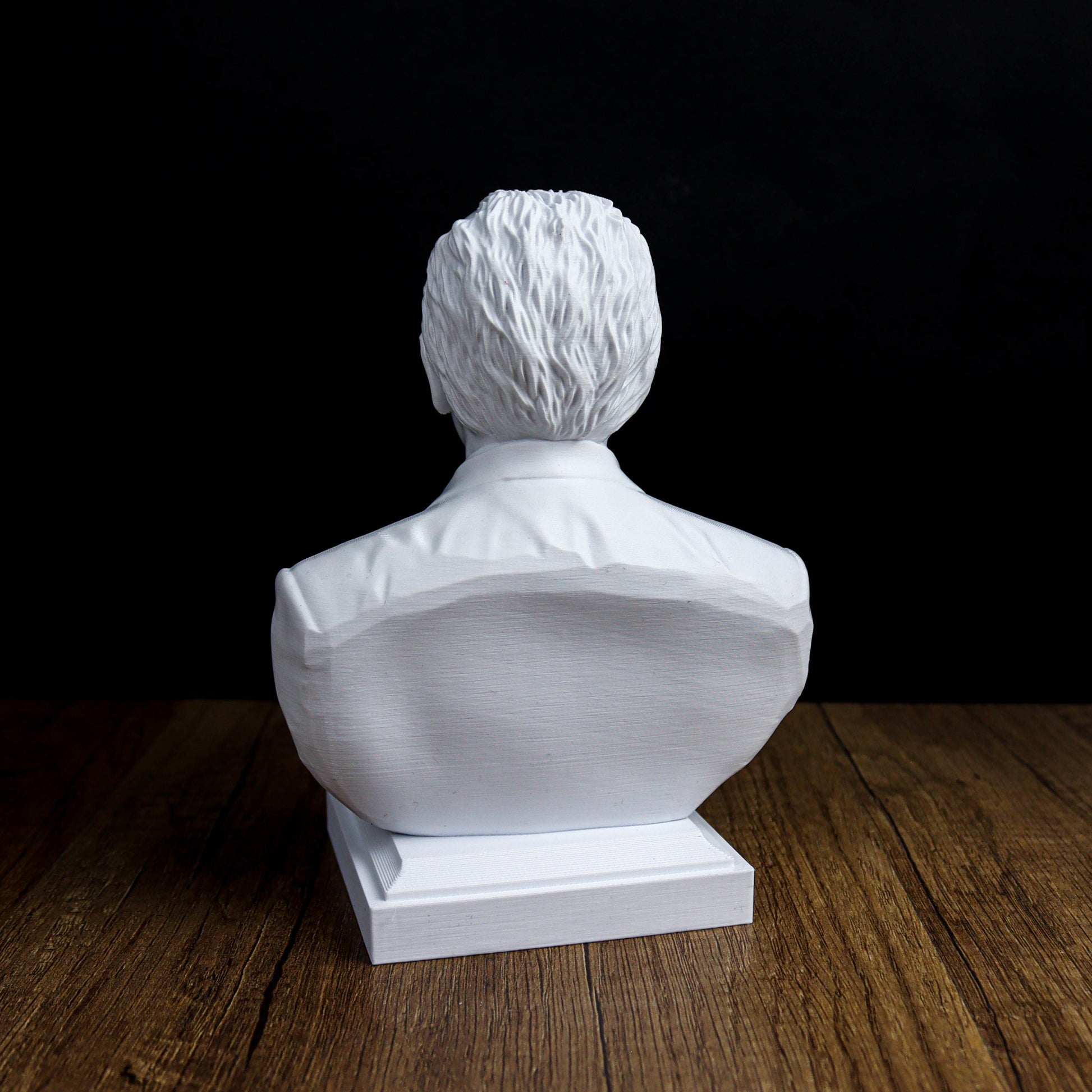 A white bust sculpture of a person sitting on a wooden surface against a black background.