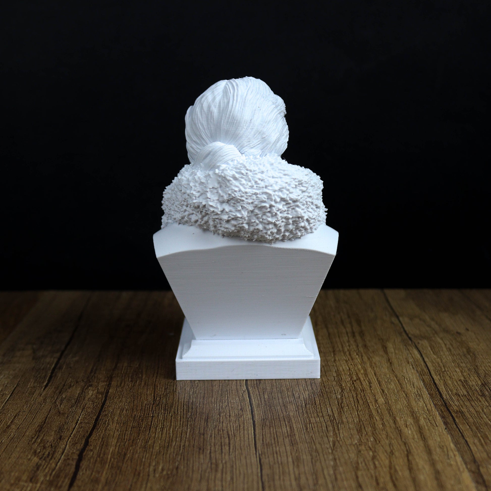 A white, 3D-printed statue of a person's head is displayed on a wooden surface against a black background.