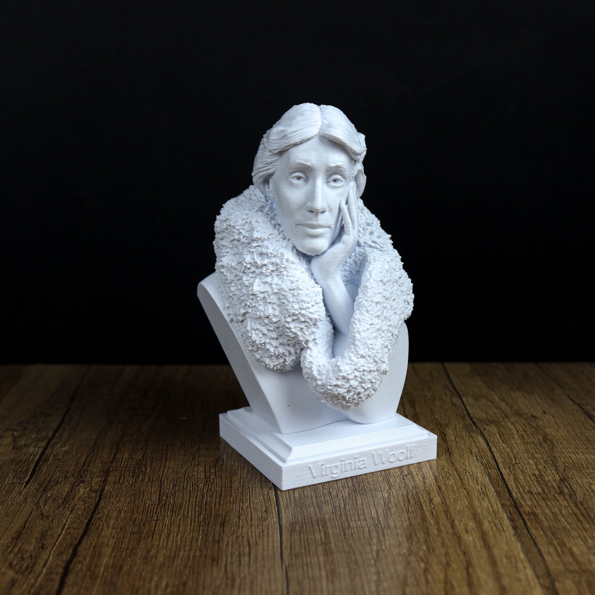 A white bust of a woman with a pensive expression, sitting on a wooden surface.