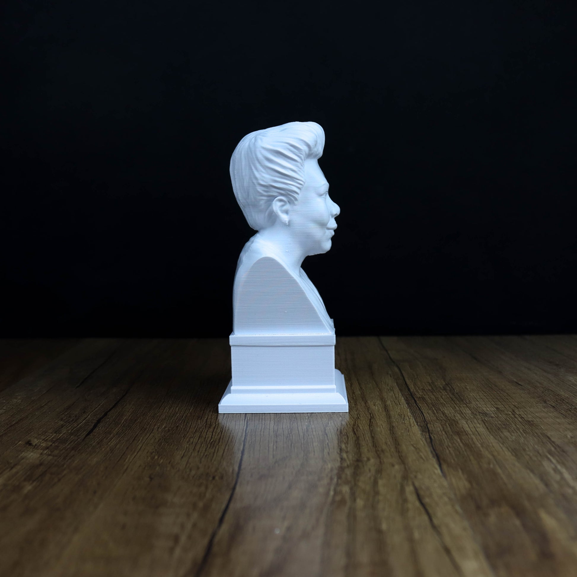 A white bust of a person is sitting on a wooden surface against a dark background.