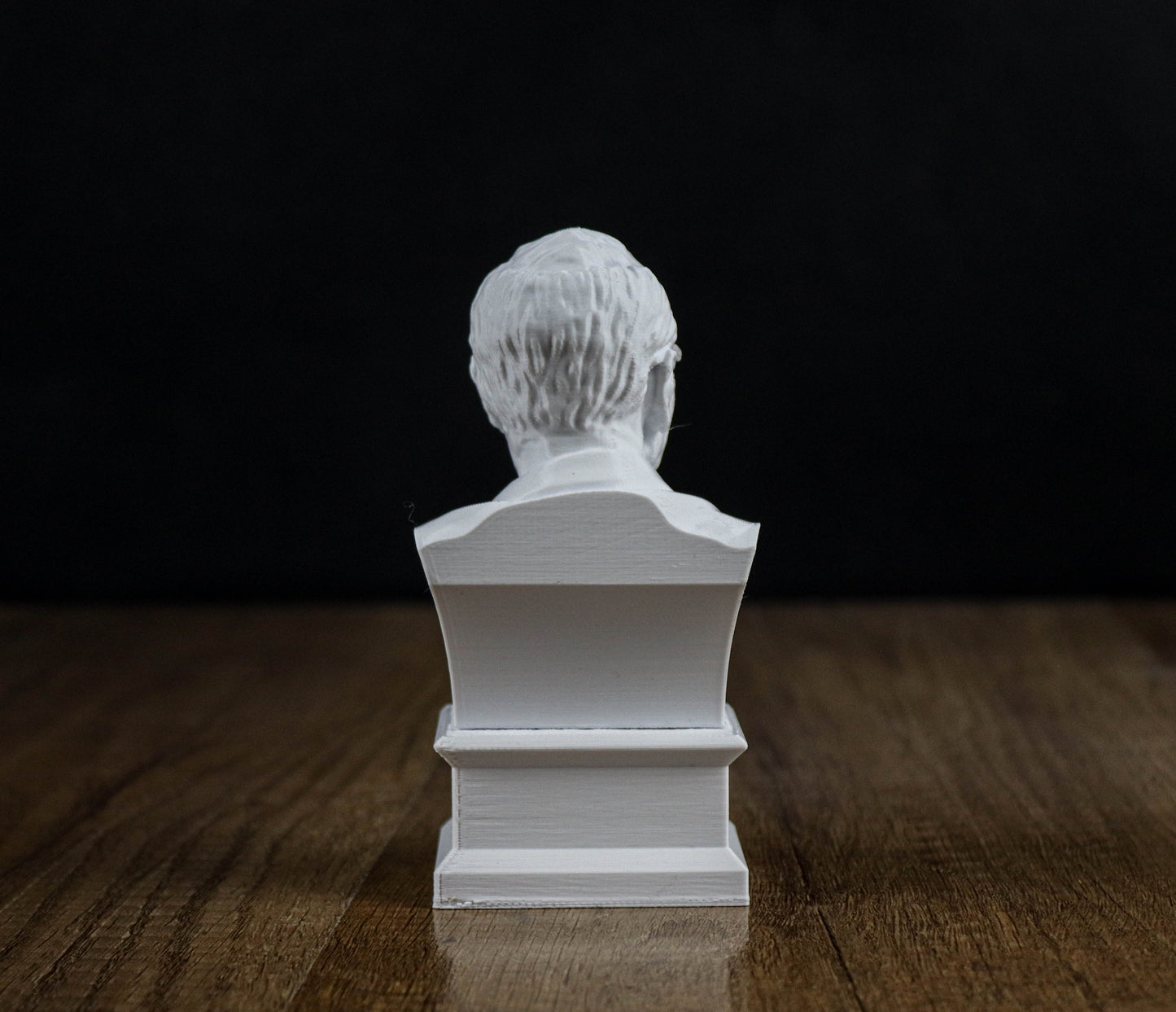A white bust of a person sitting on a wooden surface against a black background.