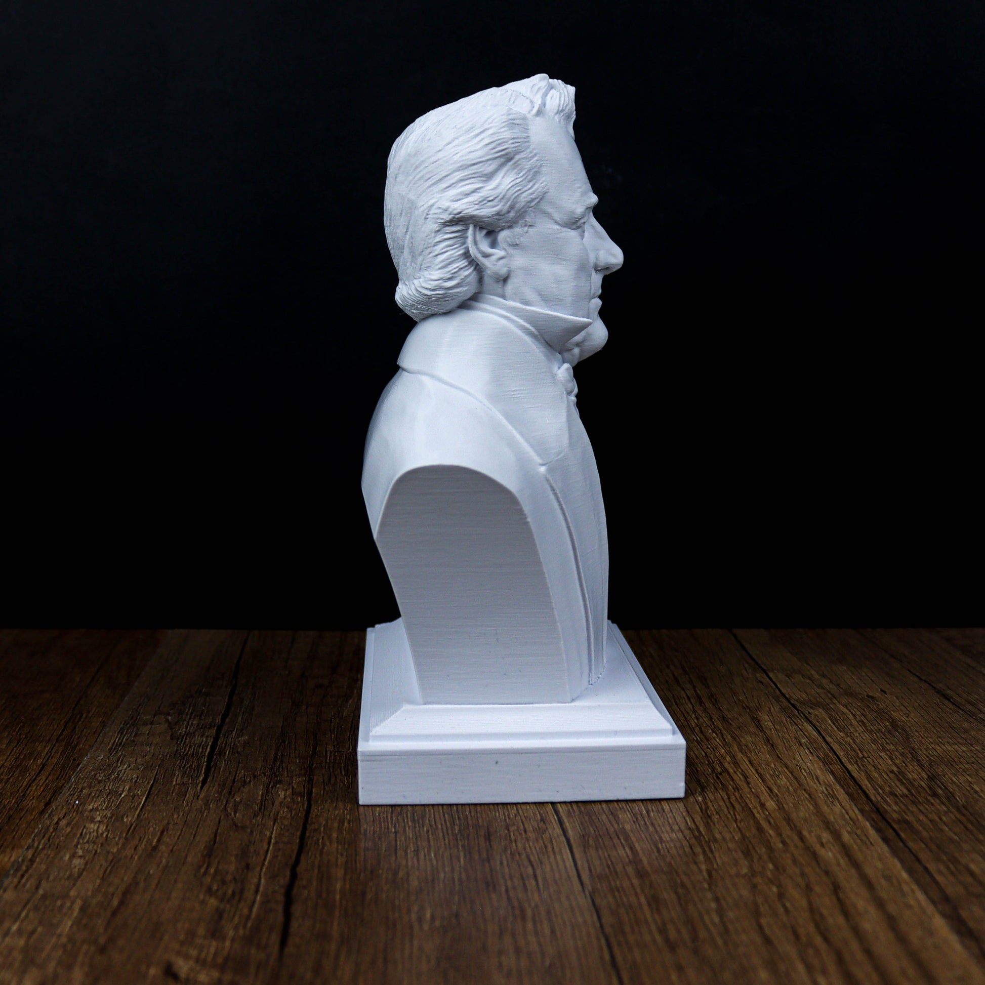 A white bust of a man is displayed on a wooden surface against a dark background.