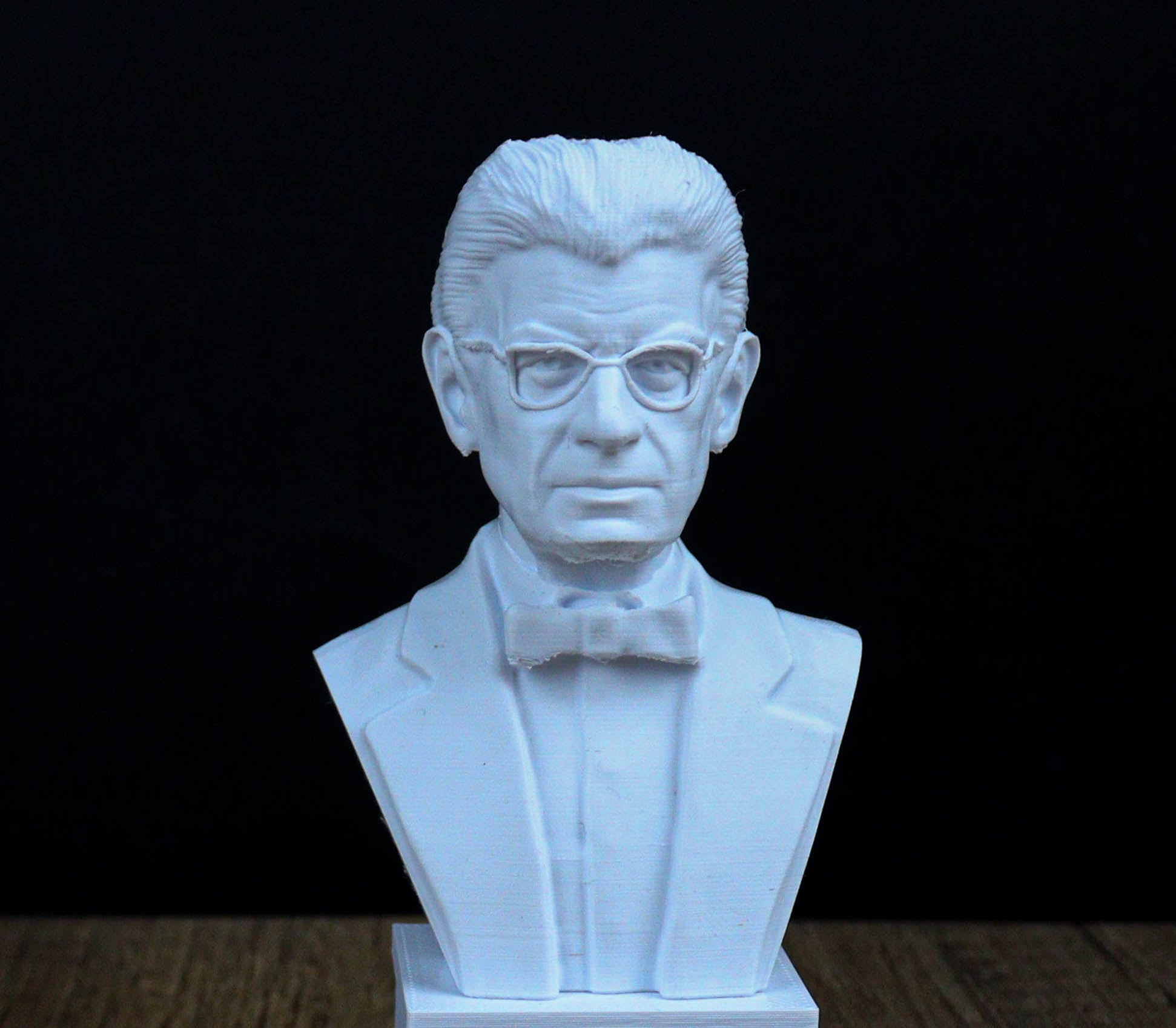 A white bust sculpture of a man wearing glasses and a suit, with a serious expression on his face.