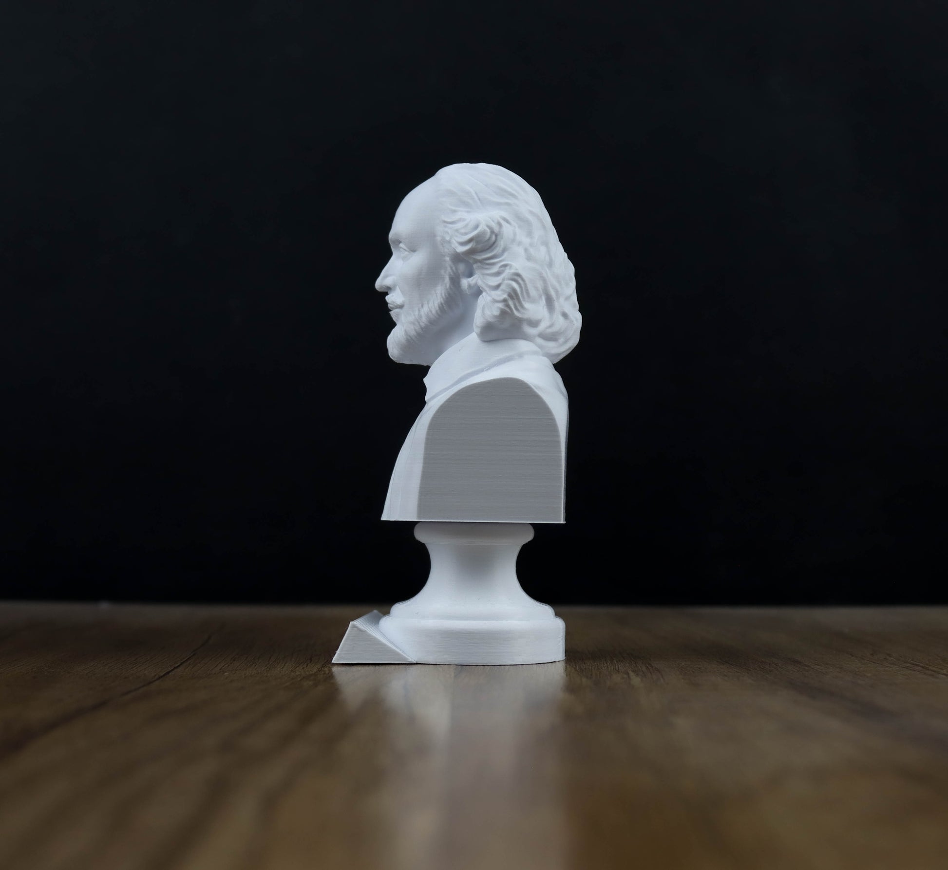 A white bust of a person is sitting on a wooden surface against a dark background.