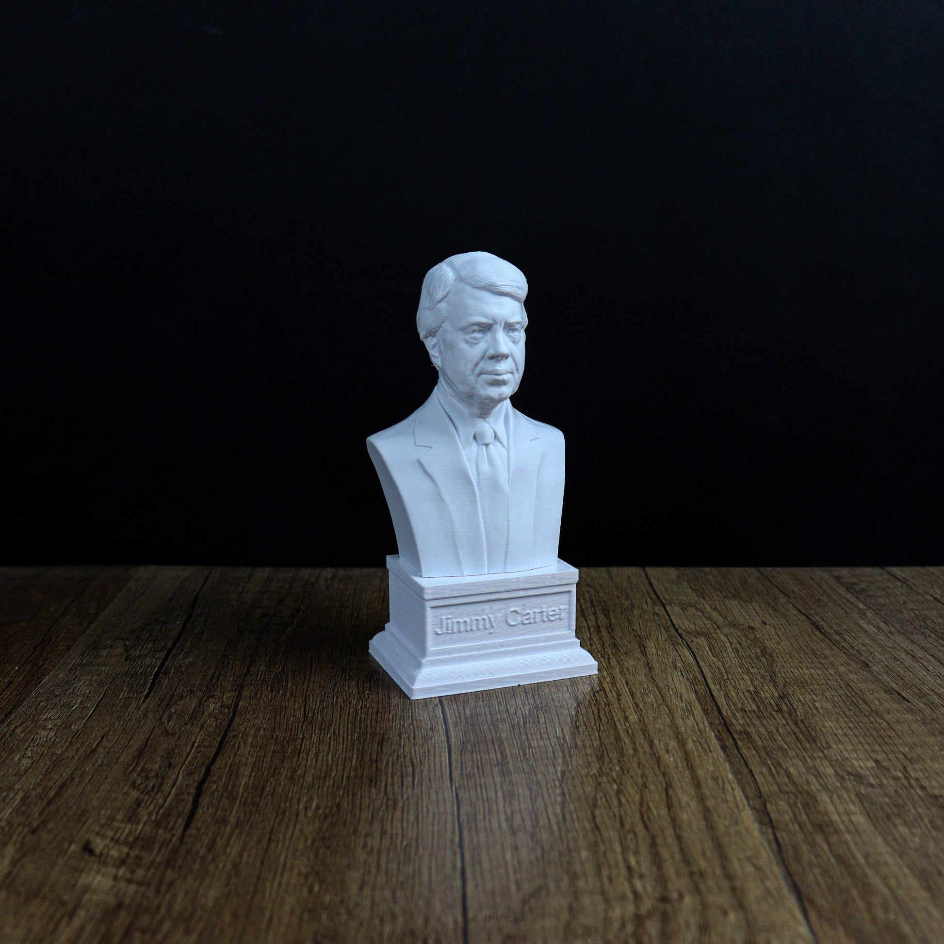 A white bust of a man, likely a historical figure, is displayed on a wooden surface against a dark background.