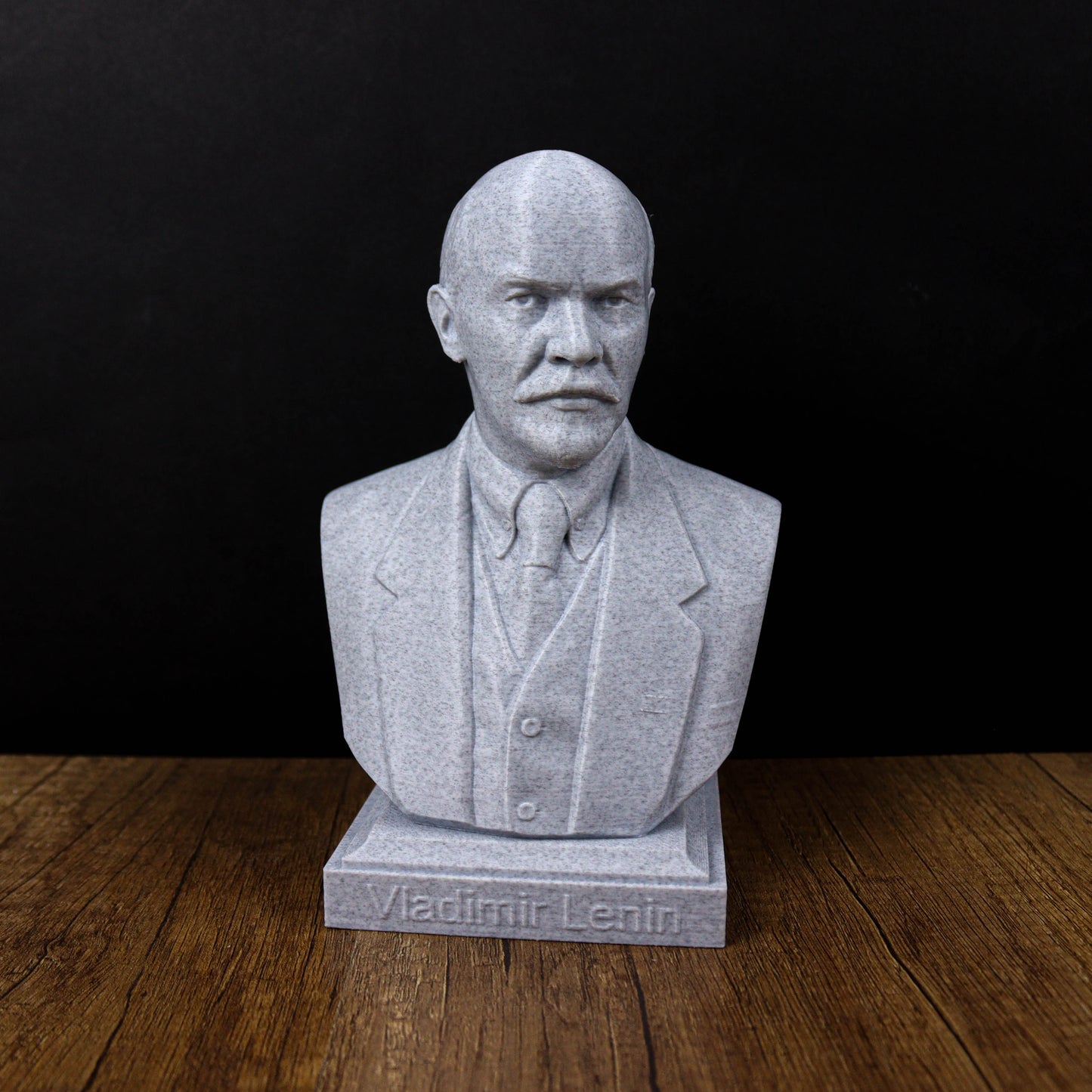 A bust of Vladimir Lenin, a prominent Russian political leader, is displayed on a wooden surface against a black background.