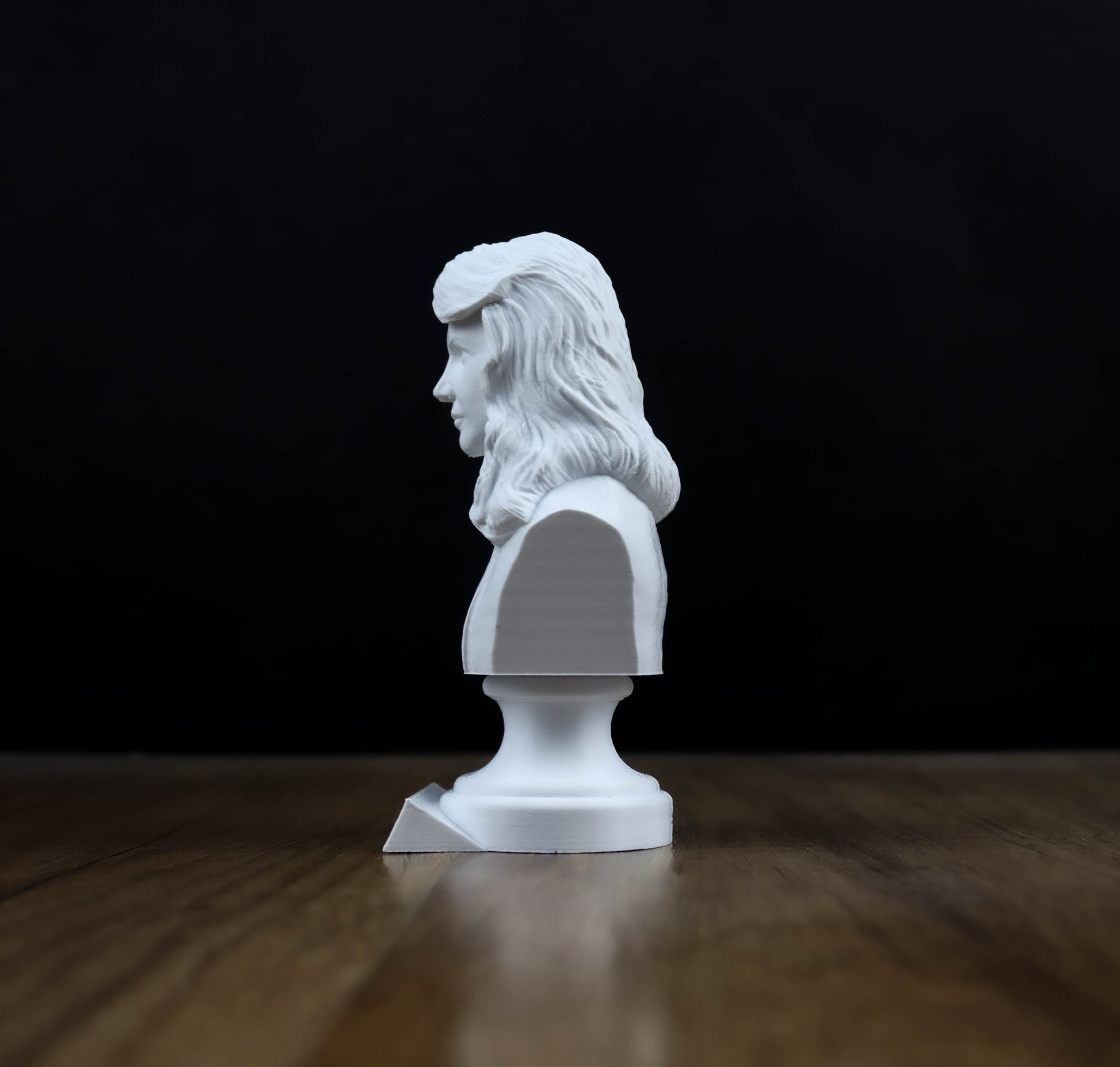 A white bust of a person is sitting on a wooden surface against a black background.