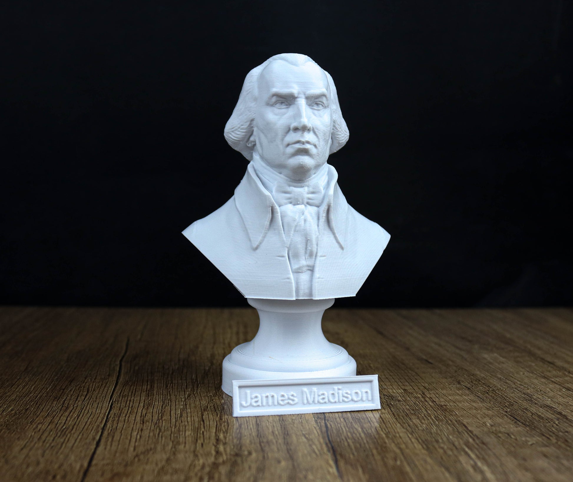 A white bust of a man, likely James Madison, is displayed on a wooden surface with a nameplate below it.