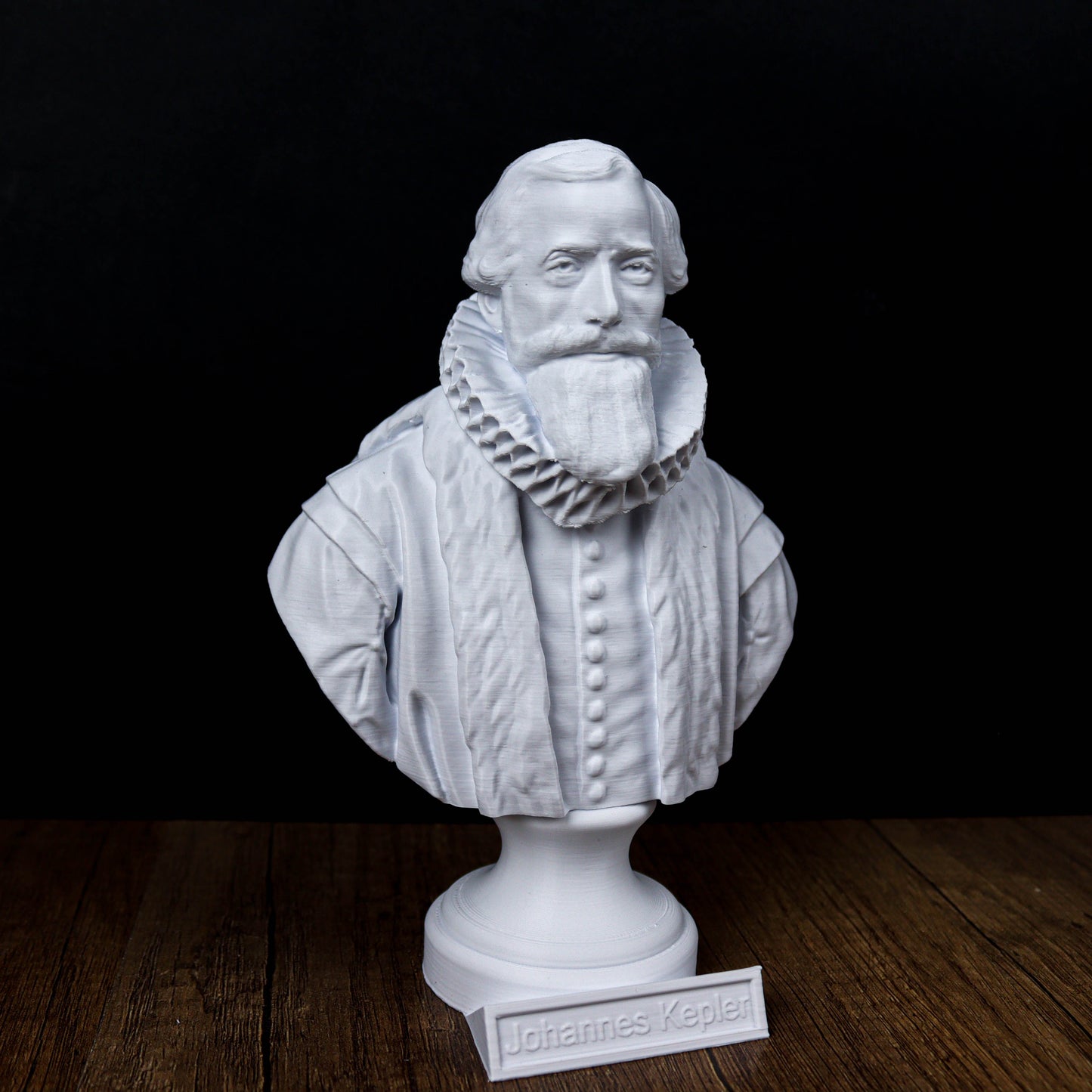 A white bust of a bearded man wearing a ruffled collar, placed on a wooden surface.