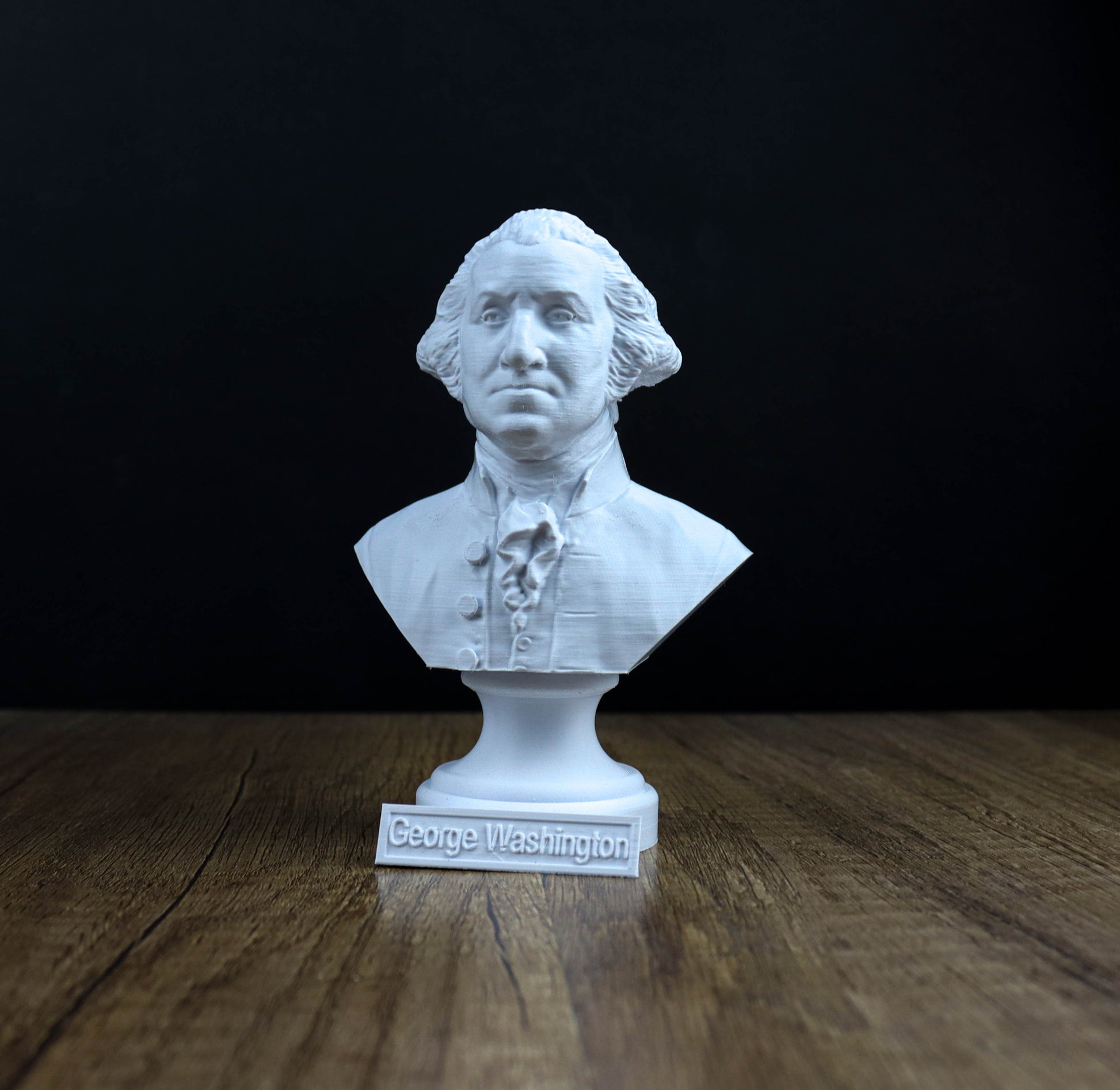 A white bust of George Washington, the first President of the United States, is displayed on a wooden surface against a black background.