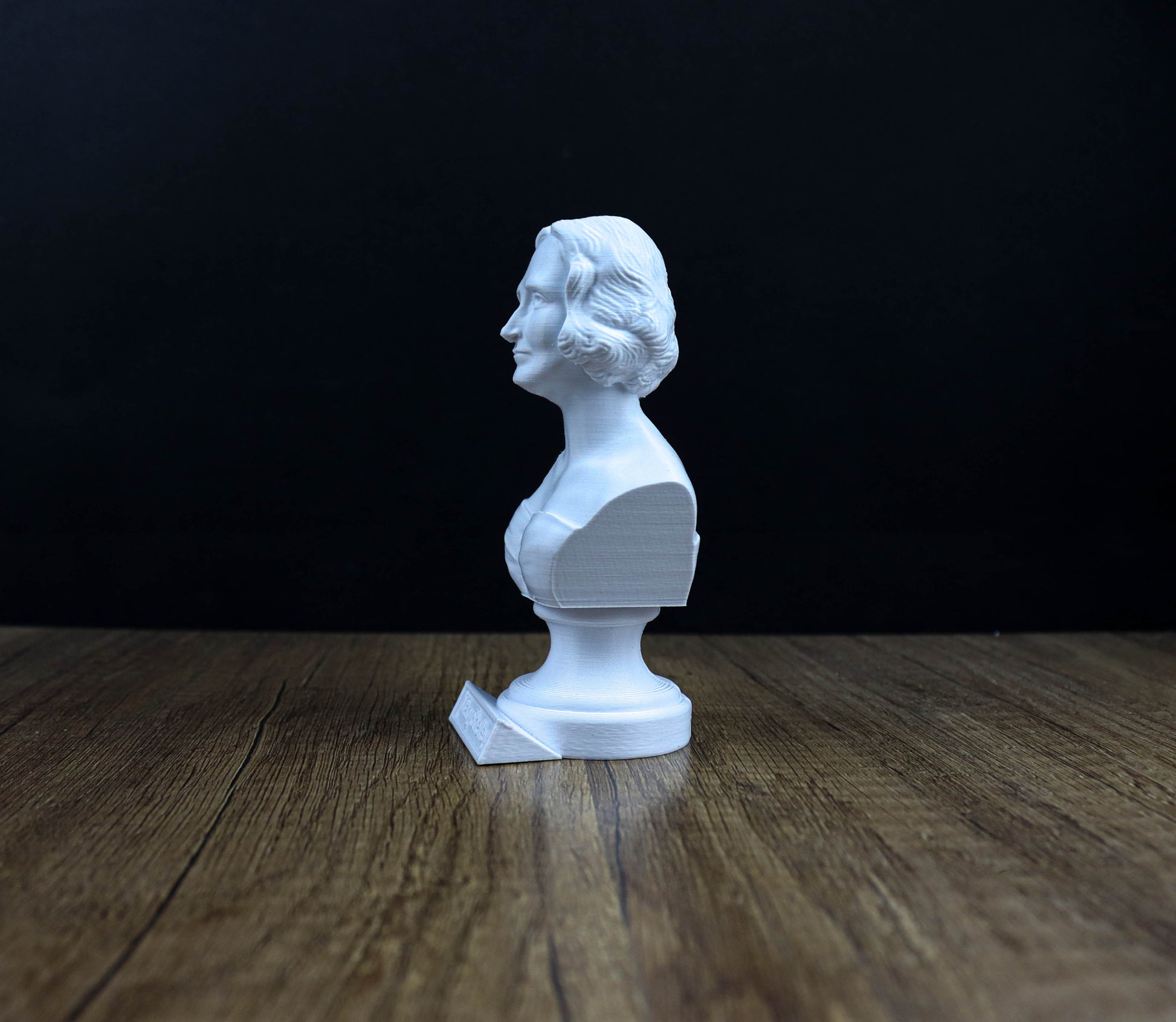 A white bust of a person is sitting on a wooden surface against a dark background.