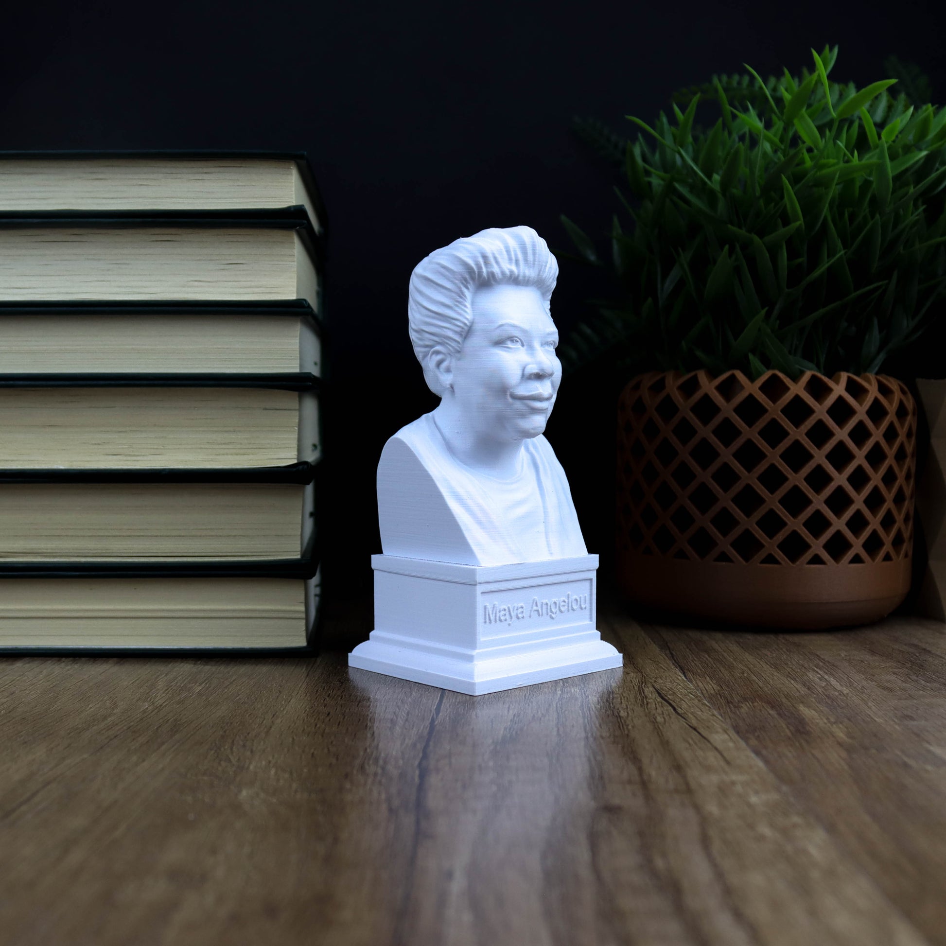 A white bust of a person is displayed on a wooden surface, surrounded by a stack of books and a potted plant.