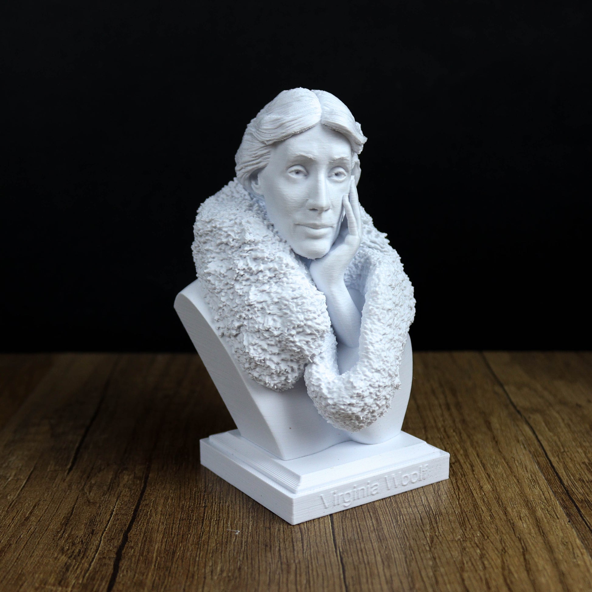 A white bust sculpture of a woman with a pensive expression, placed on a wooden surface against a black background.